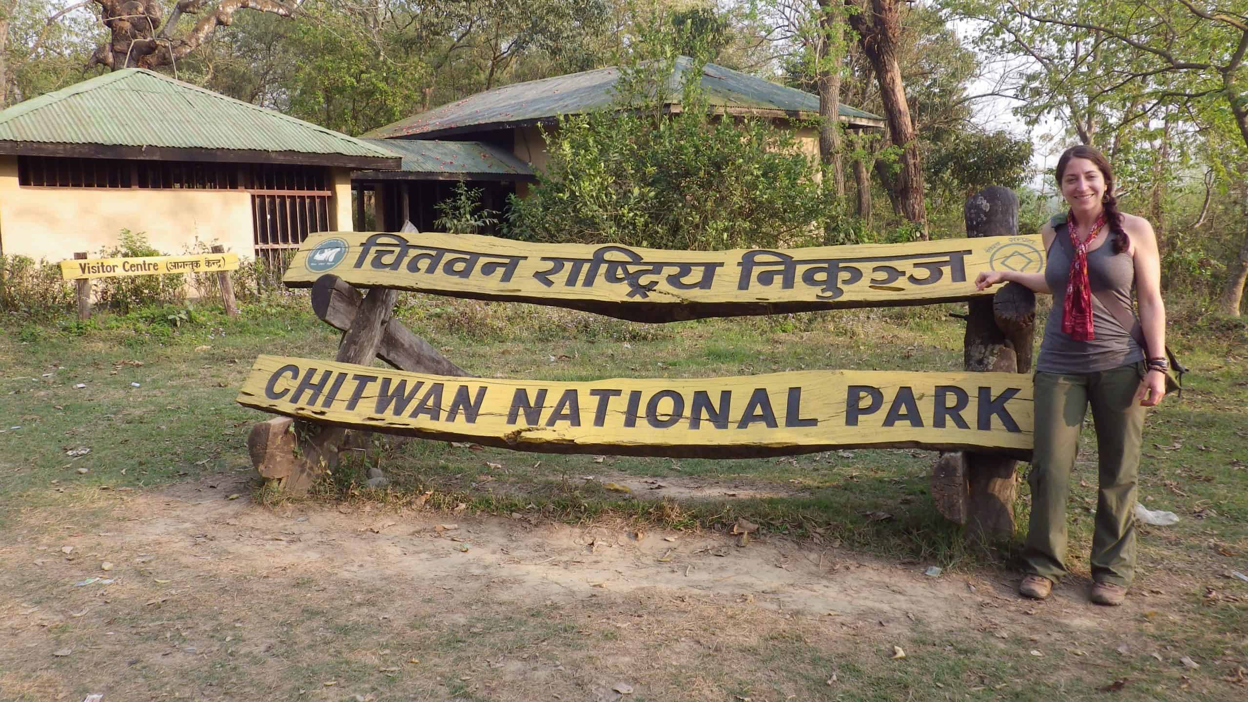 Female traveler standing beside a rustic sign for Chitwan National Park.