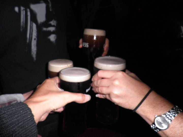 Four hands raise a Guinness in a toast in a dark pub in Dublin, Ireland.