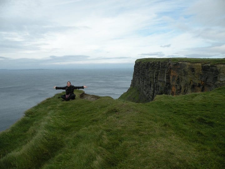 A girl sits on the edge of the Cliffs of Moher in Ireland.