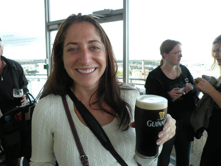 A woman in a white sweater holds a Guinness in the observatory on top of the Guinness factory in Dublin, Ireland.