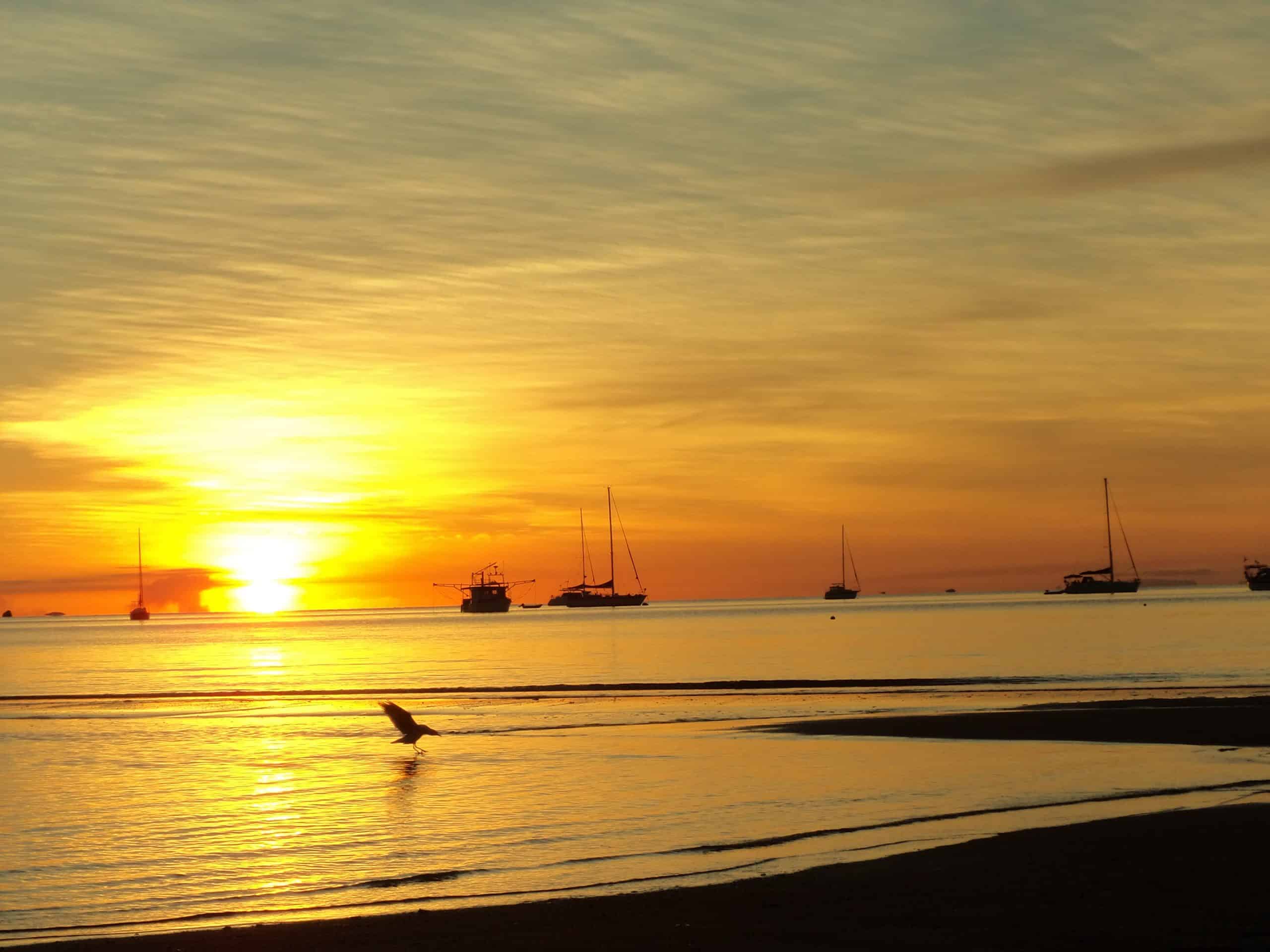 A stunning orange sunset over the water with boast floating in the distance from Magnetic Island.