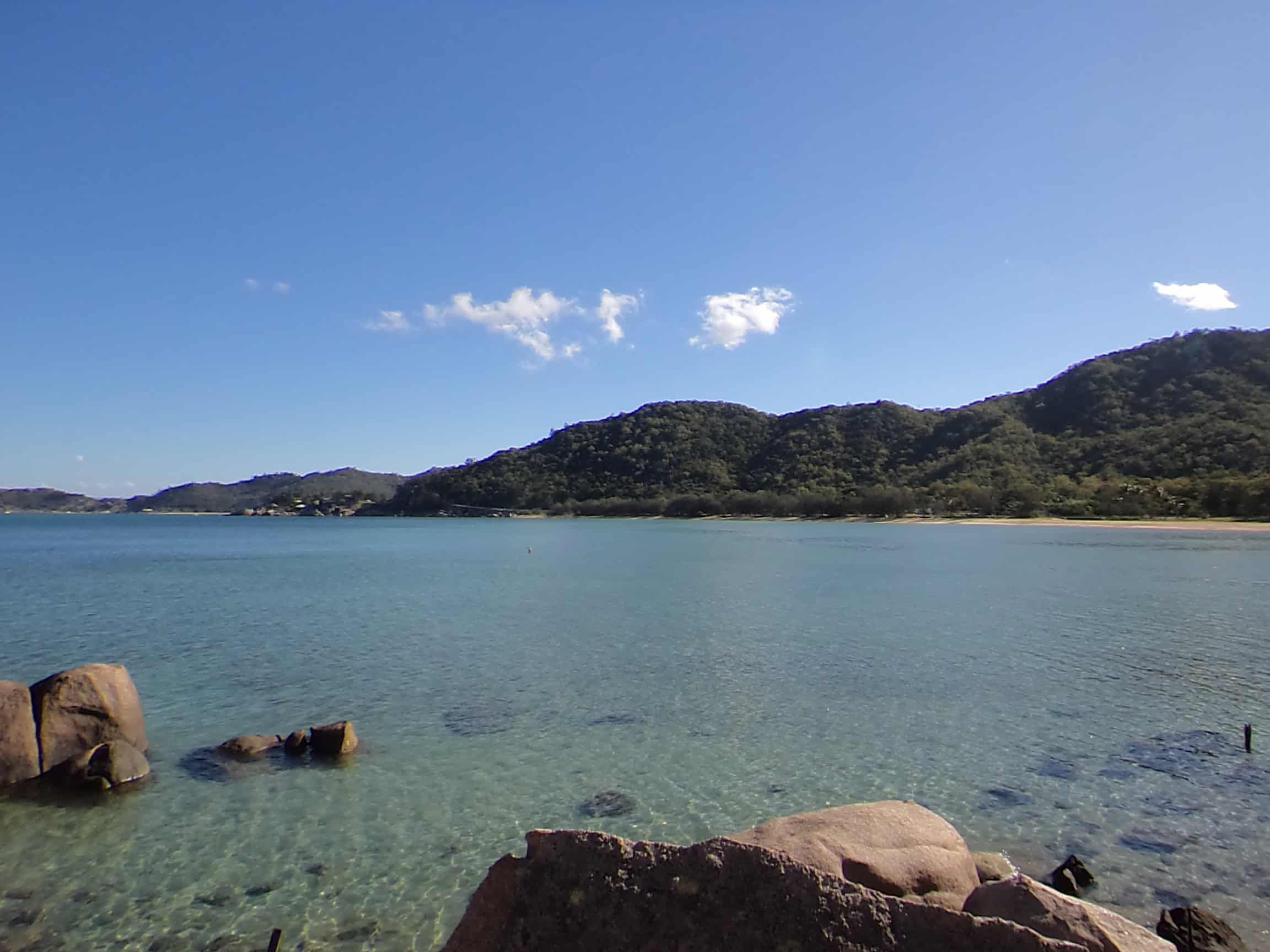 A rocky cove on Magnetic Island with still water and lush hills in the background.
