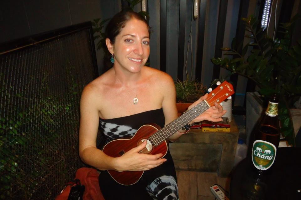 Girl sits playing the ukelele. 