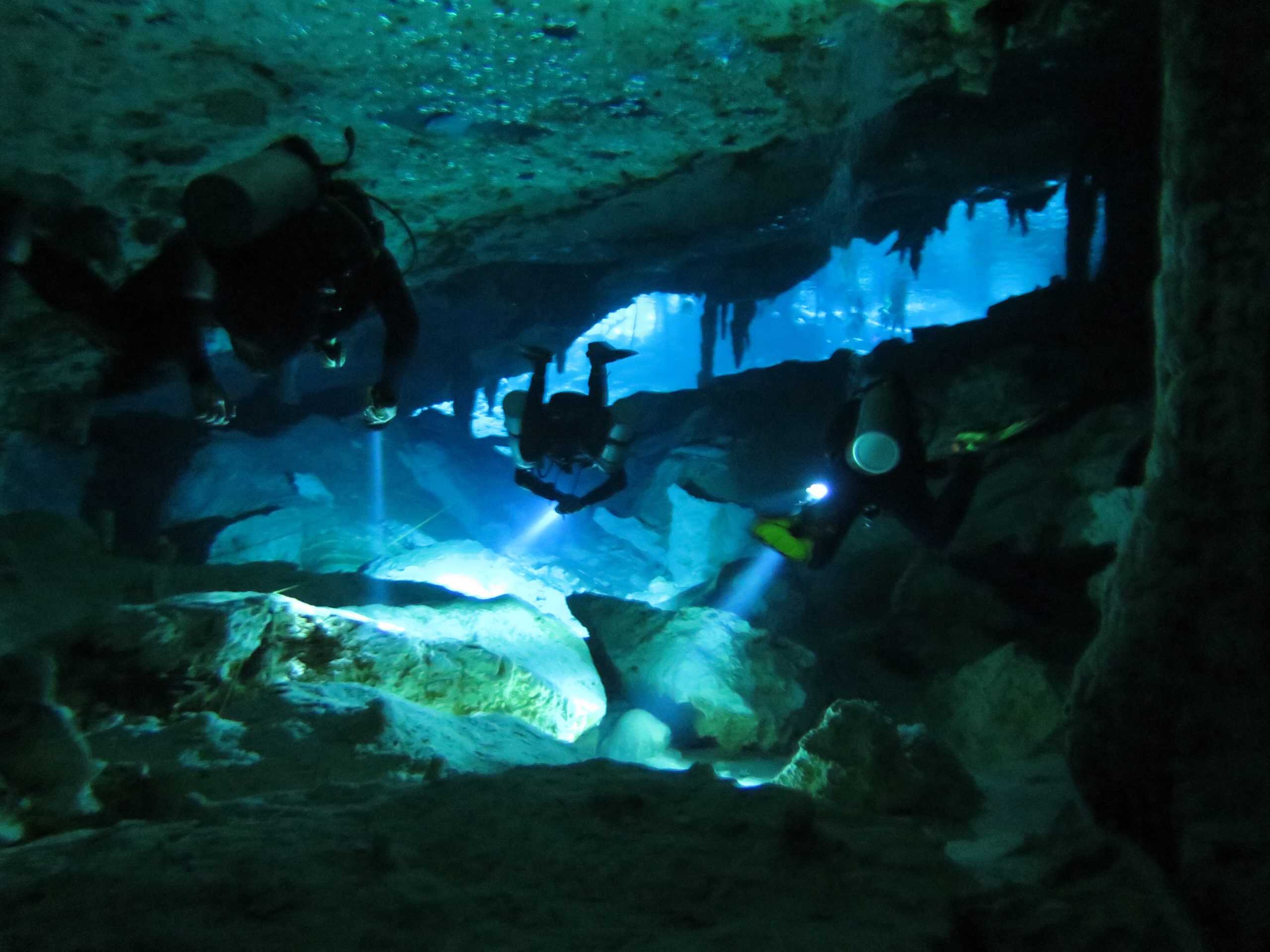 Two scuba divers swim towards the cavern entrance of Dos Ojos cenote in Tulum, Mexico.
