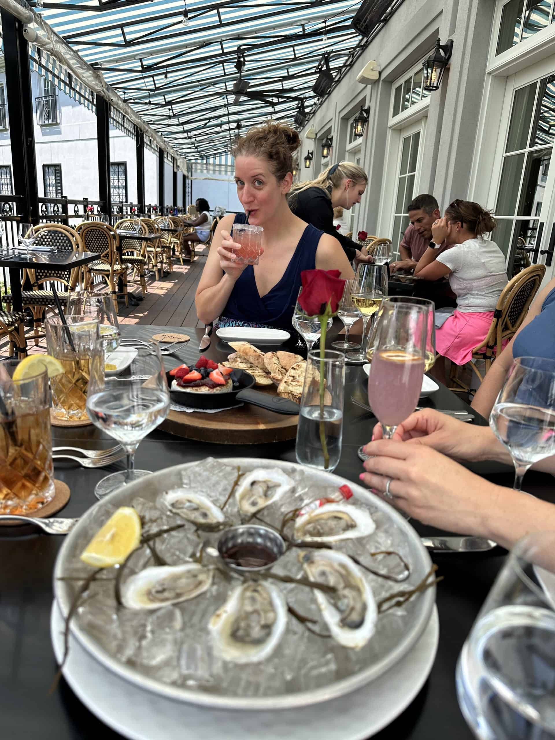 A woman sips a cocktail with appetizers on the table in front of her.