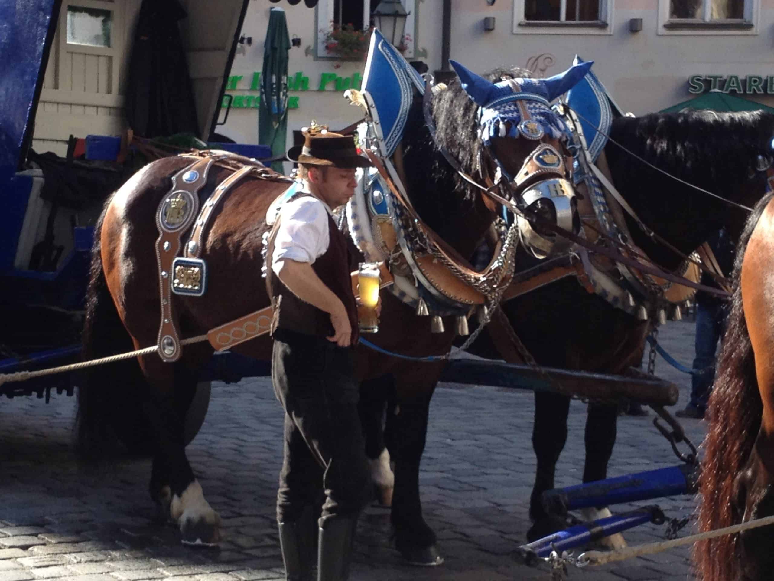Horses pulling an Oktoberfest beer cart and their keeper dressed for Oktoberfest.