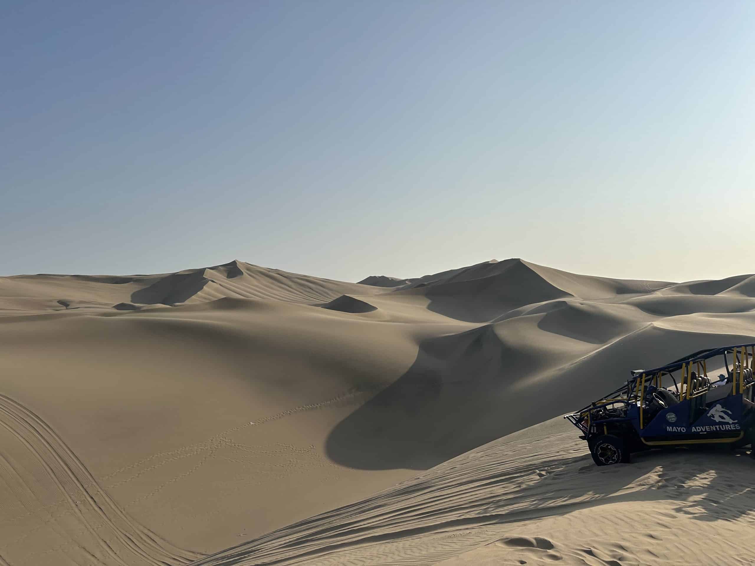 A dune buggy sits on the top of a sandy dune with the vast desert spreading out before it.