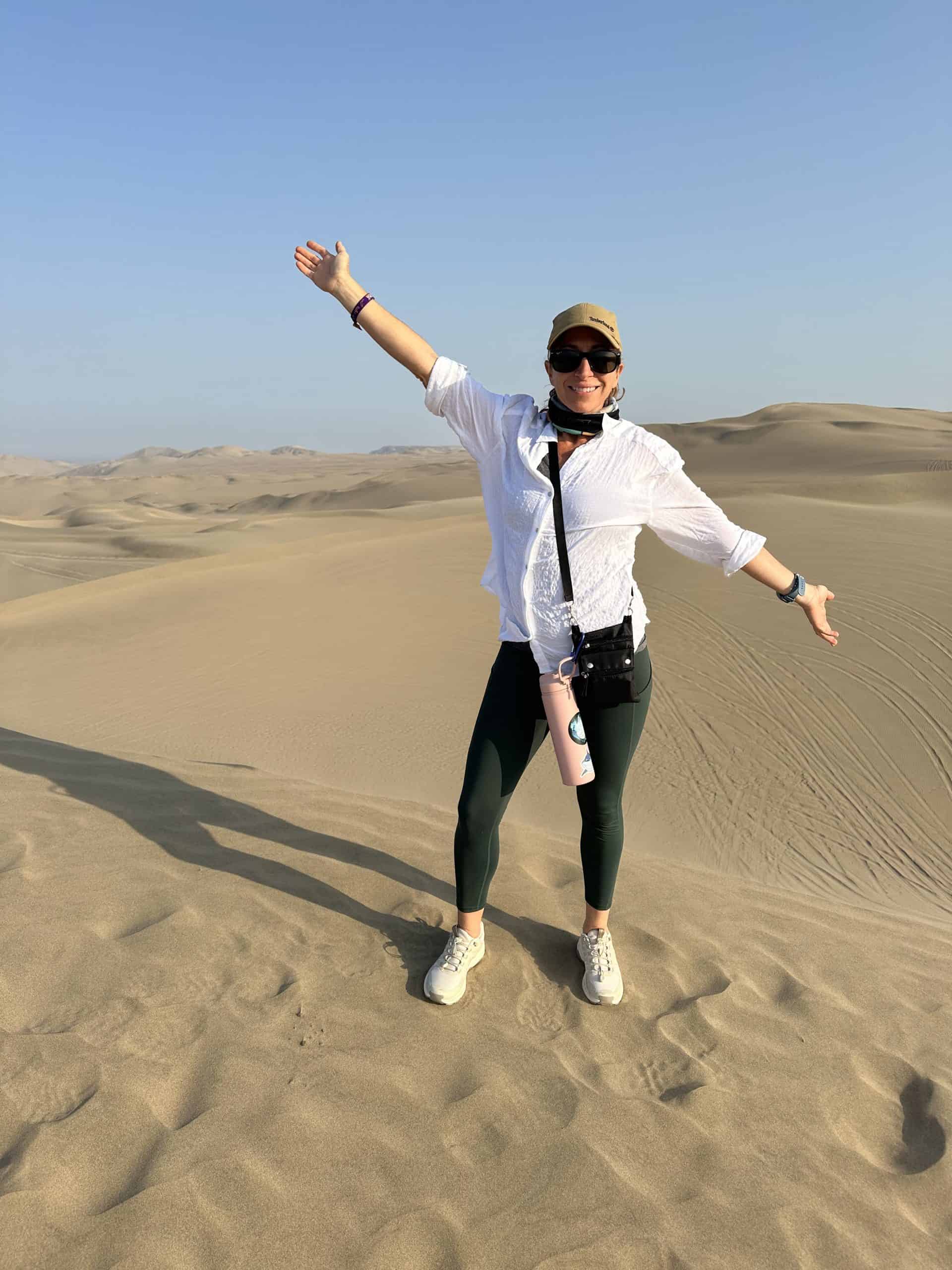 Woman on a Huacachina Oasis tour from Lima stands with arms spread wide in the Ica Desert.