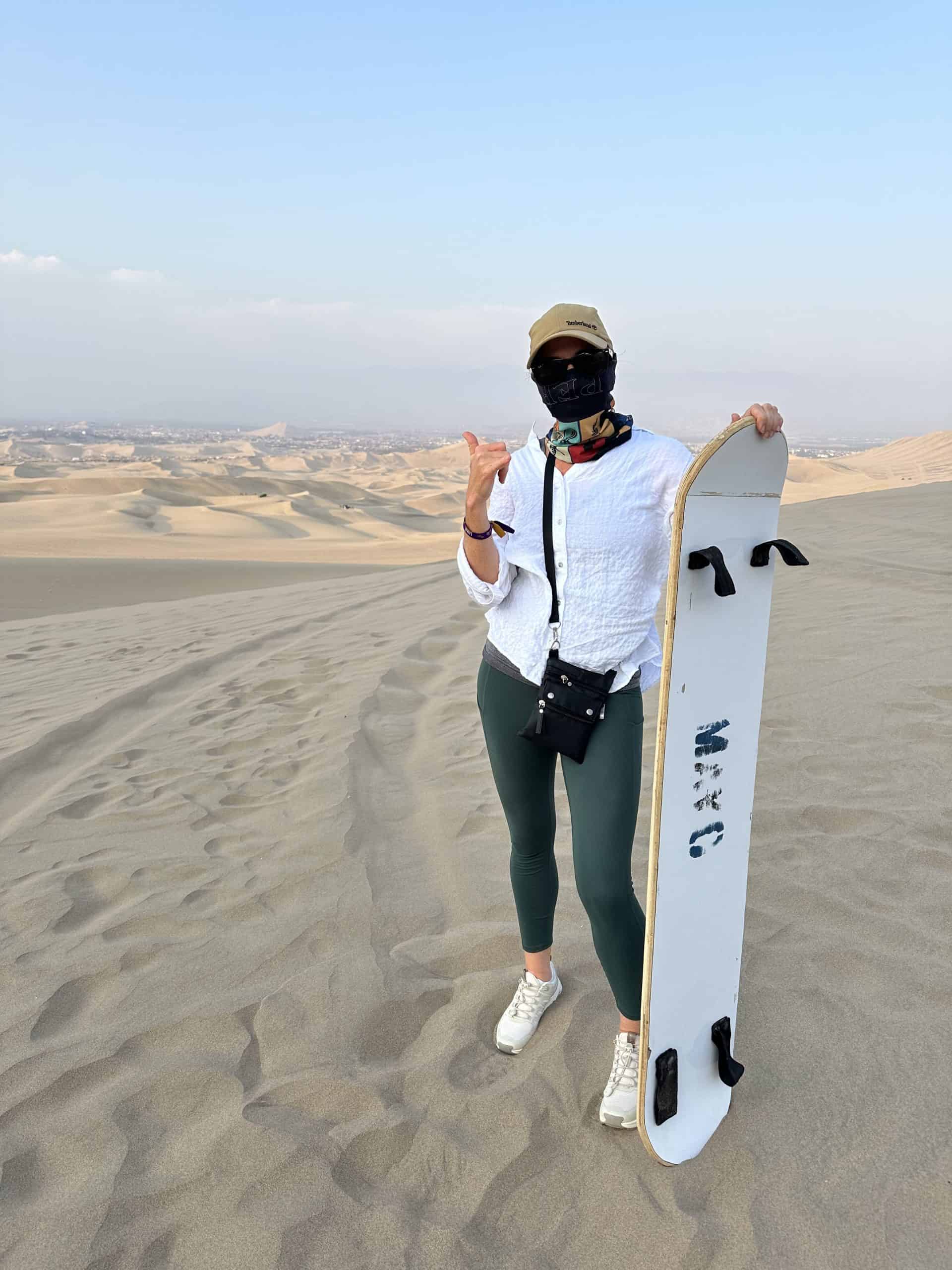 A woman is ready to go sandboarding on her Huacachina Oasis tour with her sunglasses, face scarf and board.
