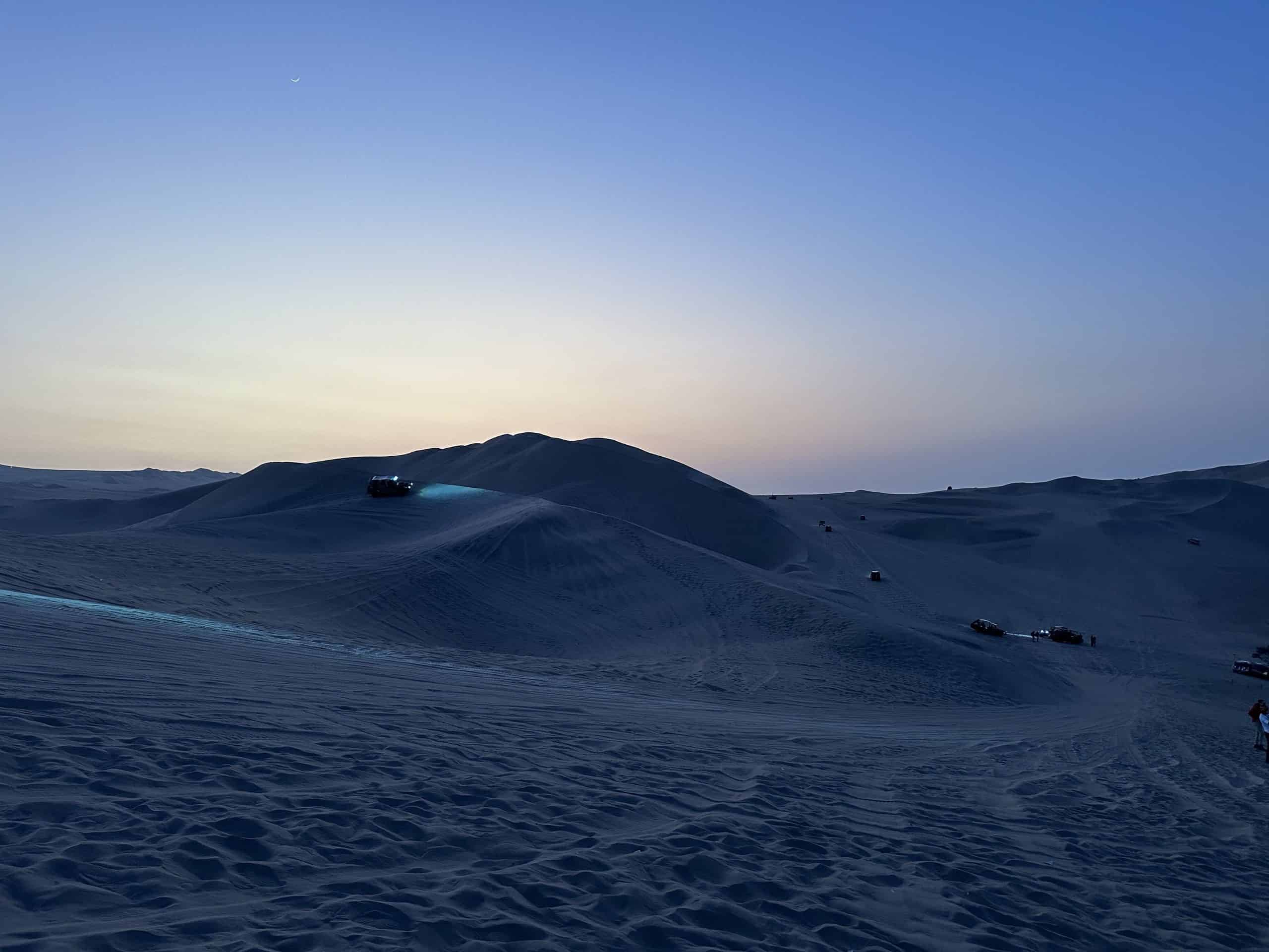 Dune buggies continue to surf the dunes while the last hint of sun kisses the sand in Huacachina Oasis.