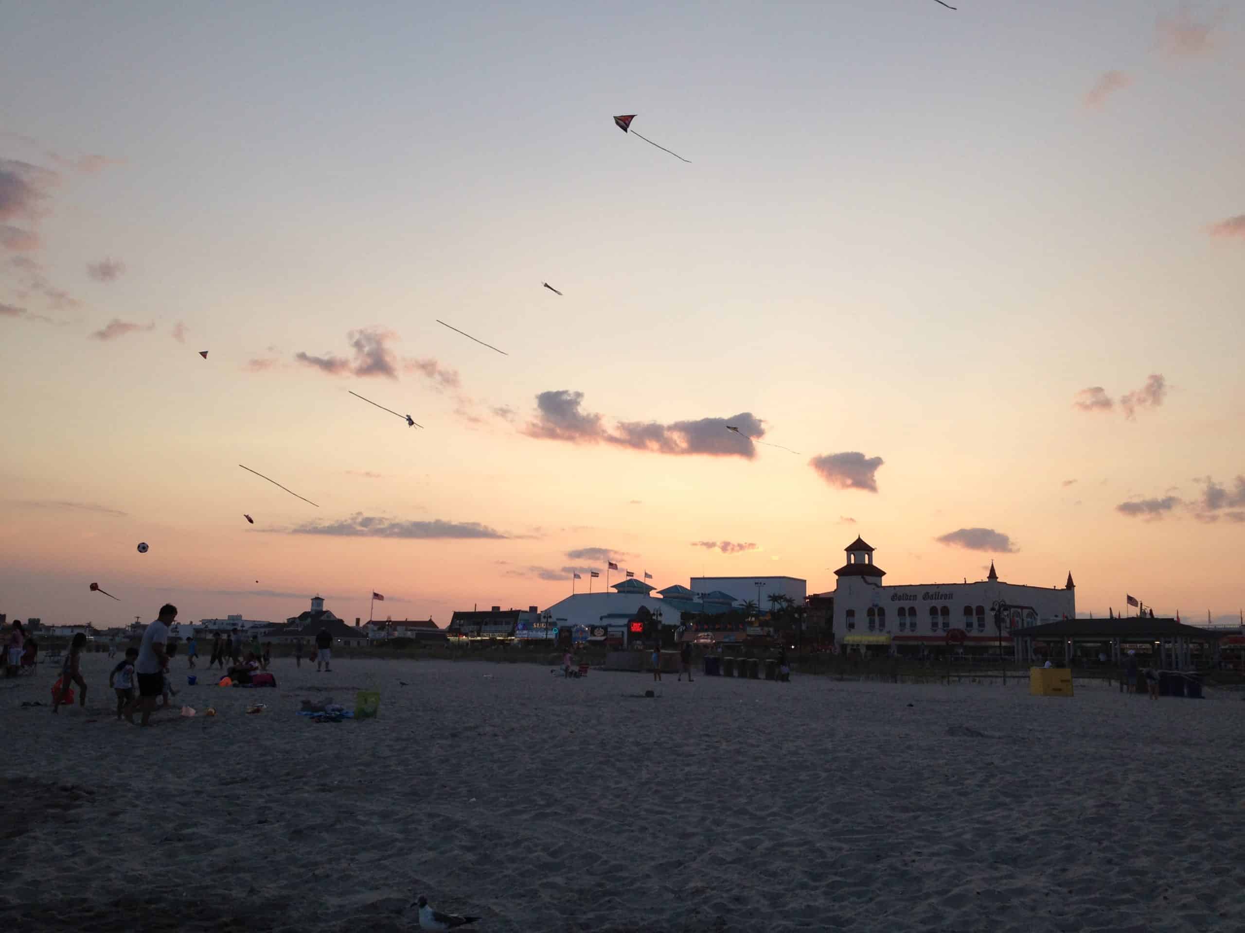 Kites being flown at the OCNJ beach at dusk with the boardwalk silhouetted in the background.