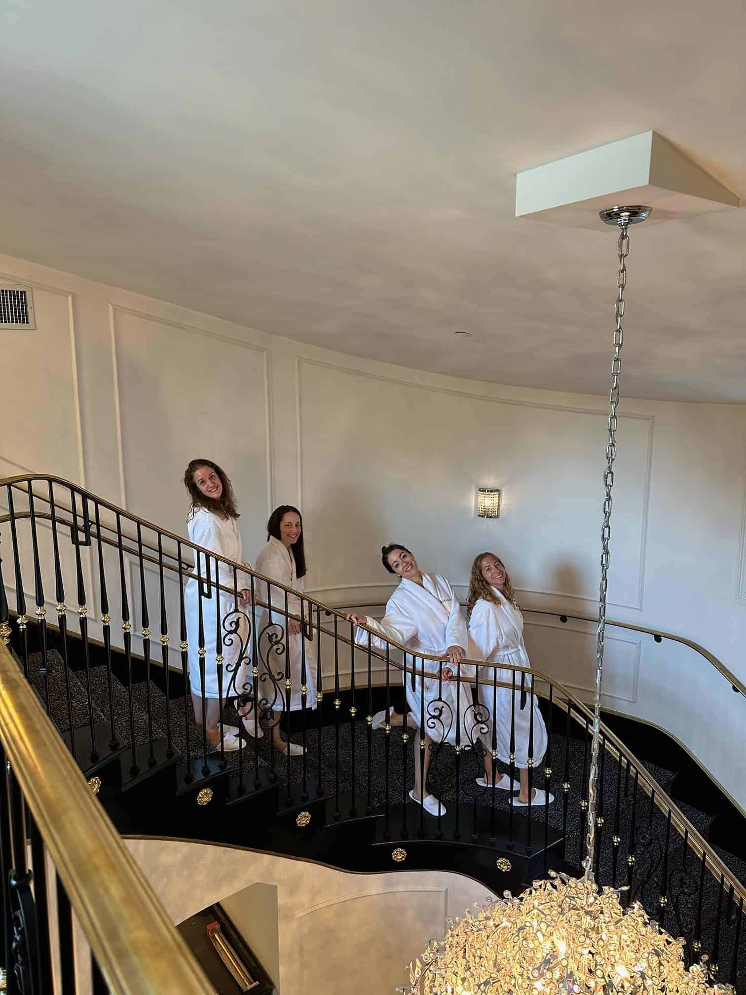 Four women in robes descend a spiral staircase towards the spa at Mirbeau resort in Rhinebeck, NY.