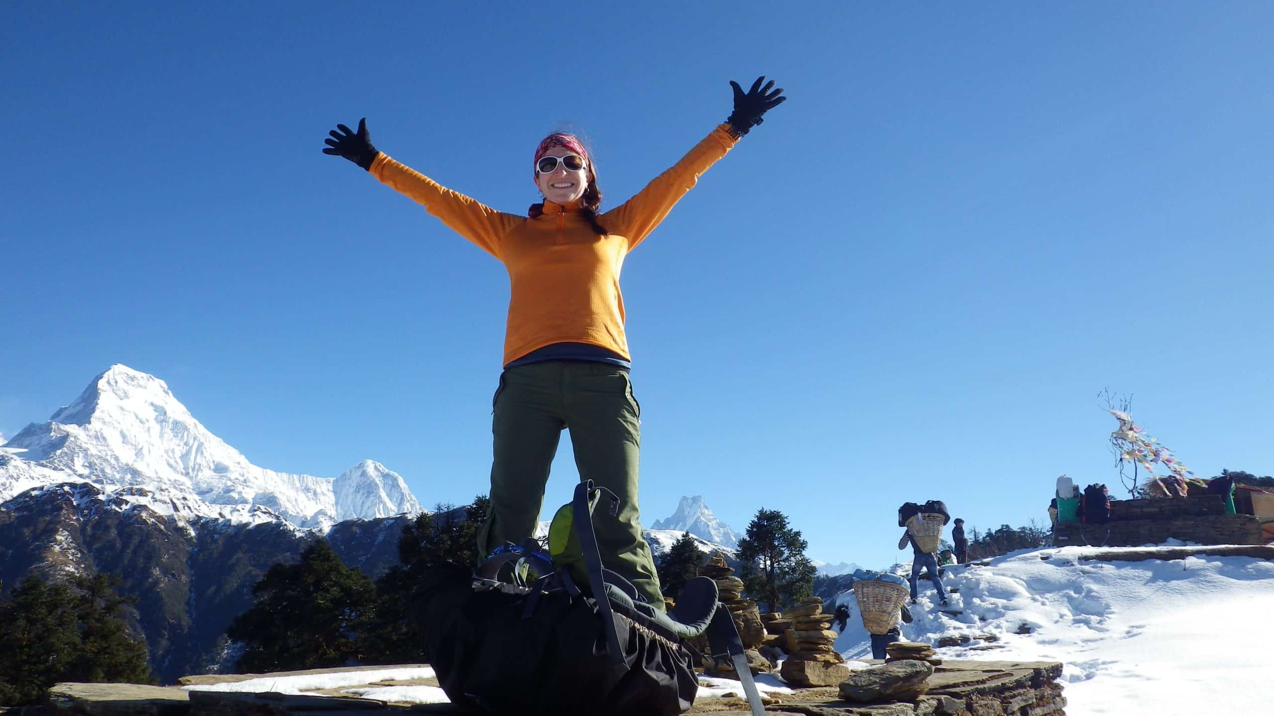 A trekker on the Annapurna Circuit poses triumphantly with snowy mountains in the background.