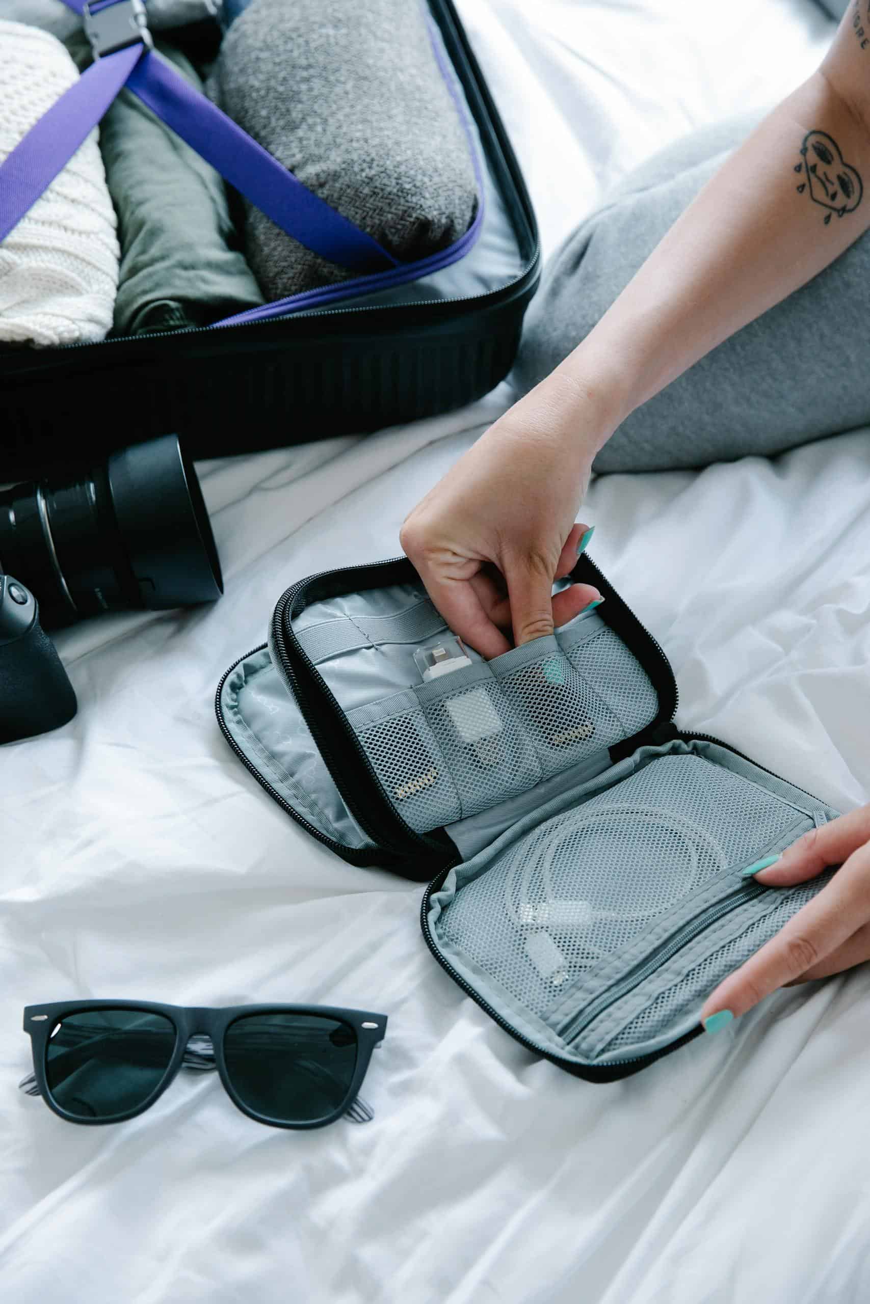 Close-up view of travel essentials including an electronics organizer on a bed.