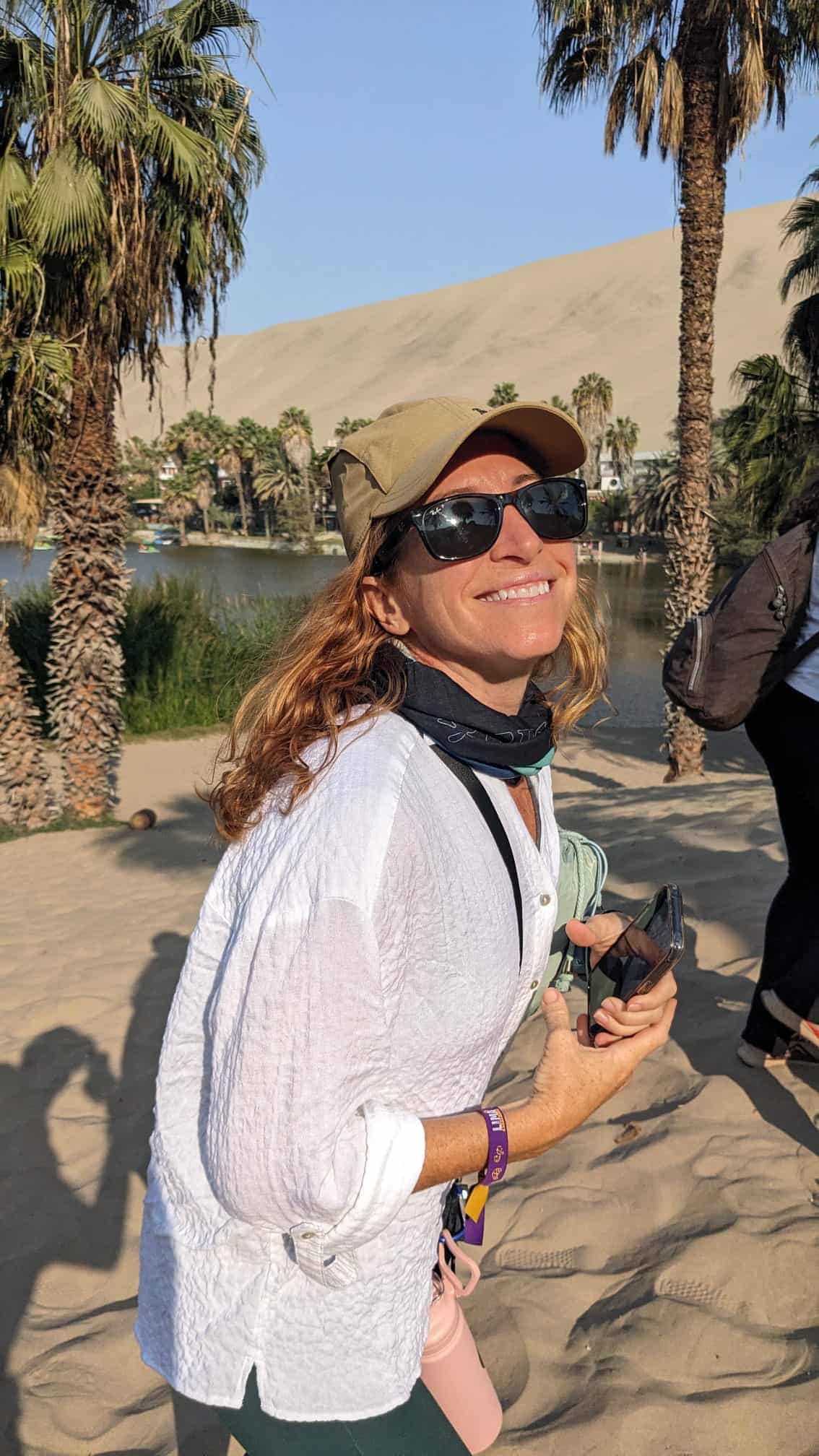 A woman walks up the desert dunes with Huacachina Oasis in the background.