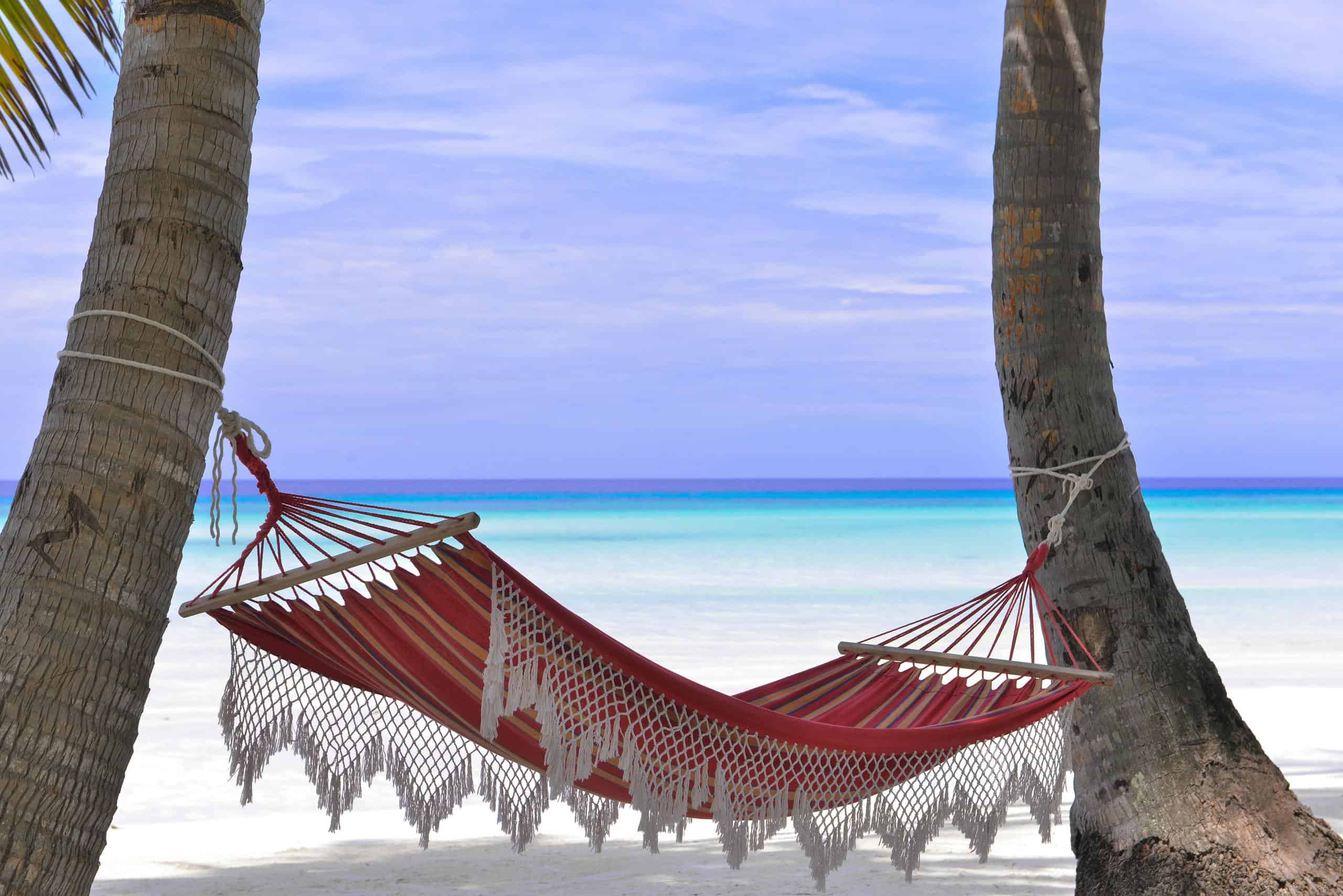 Idyllic beach hammock in the Eastern Caribbean between coconut trees with azure, blue waters.