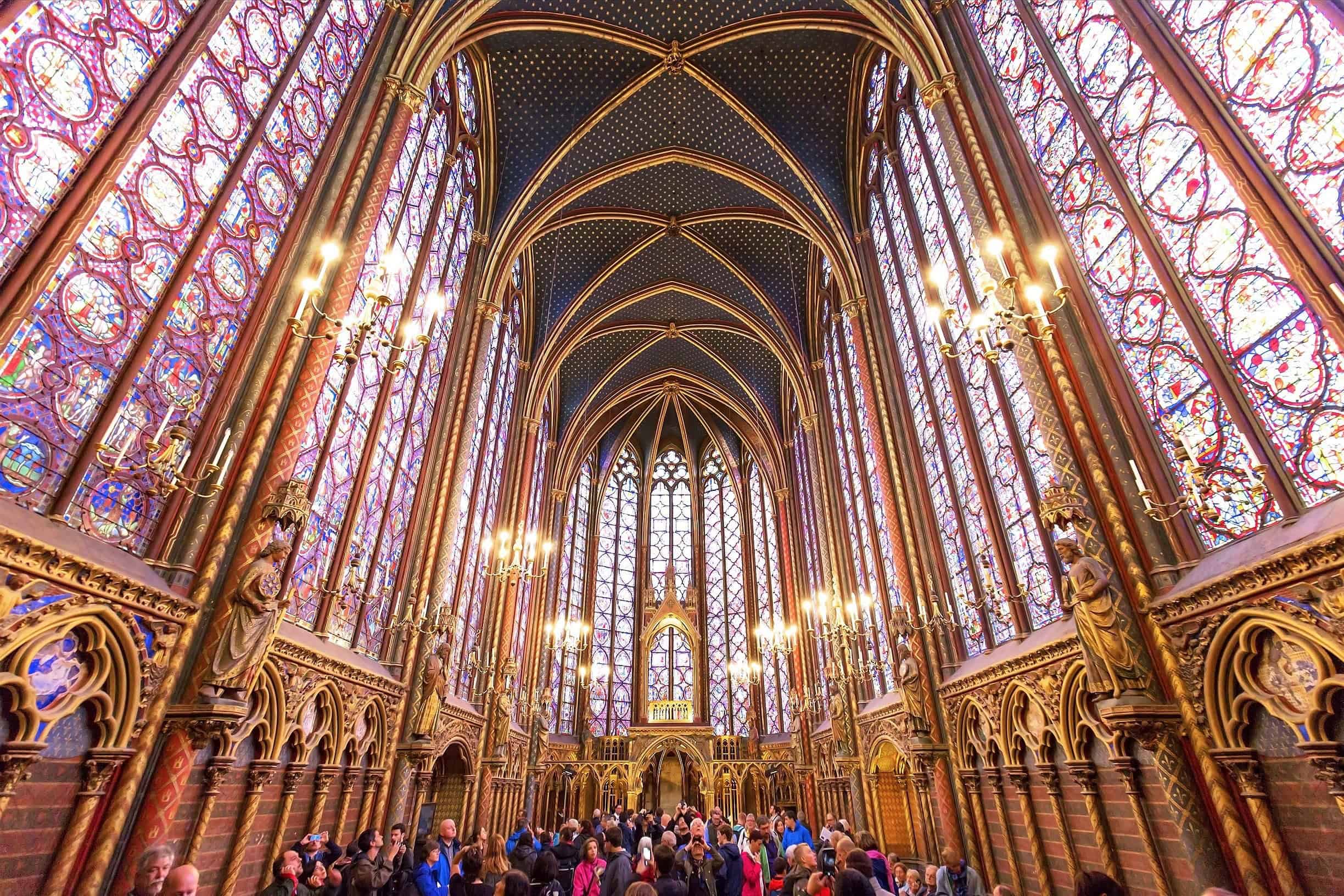 The inside of the Le Sainte Chapelle in Paris, France, with sun streaming through stained-glass windows illuminating the interior.