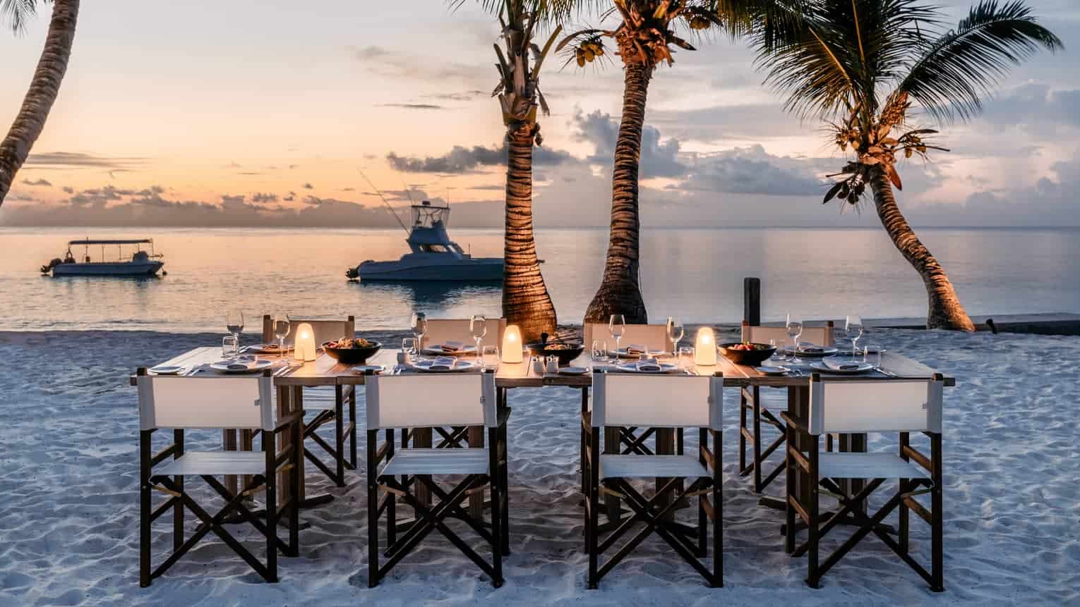 A beachside candlelit dining table overlooking a calm sea at dusk on the Seychelles islands.