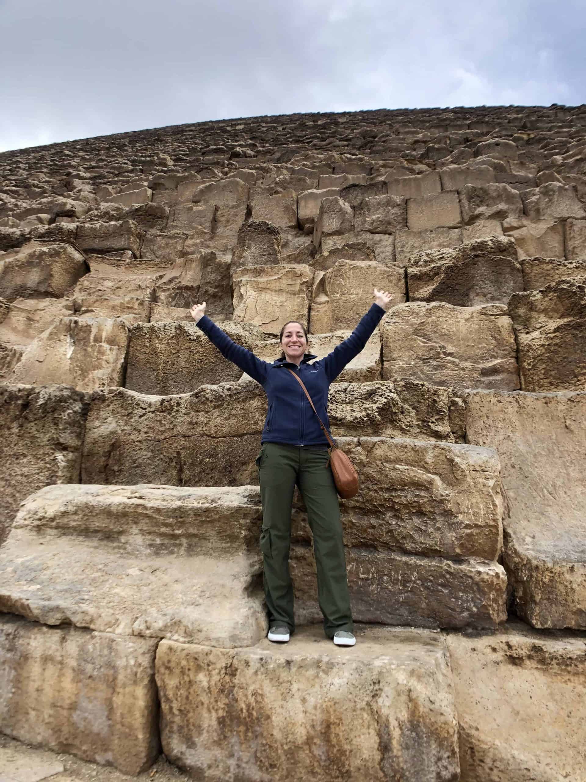 Woman stands on and is dwarfed by the blocks of the Great Pyramid of Giza in Cairo, Egypt.