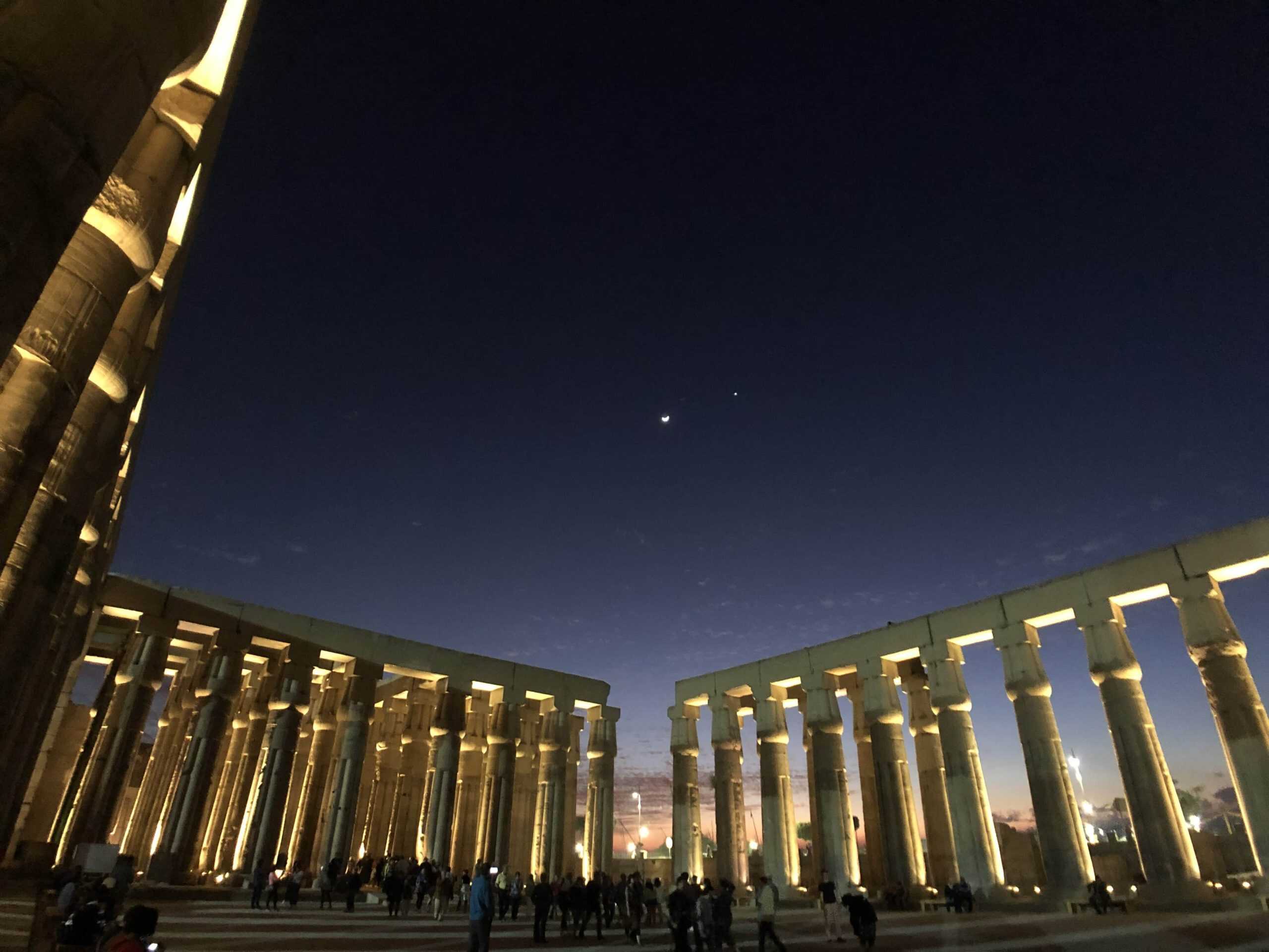 The stars and moon begin to rise over the stone pillars at the Temple of Luxor in Egypt.