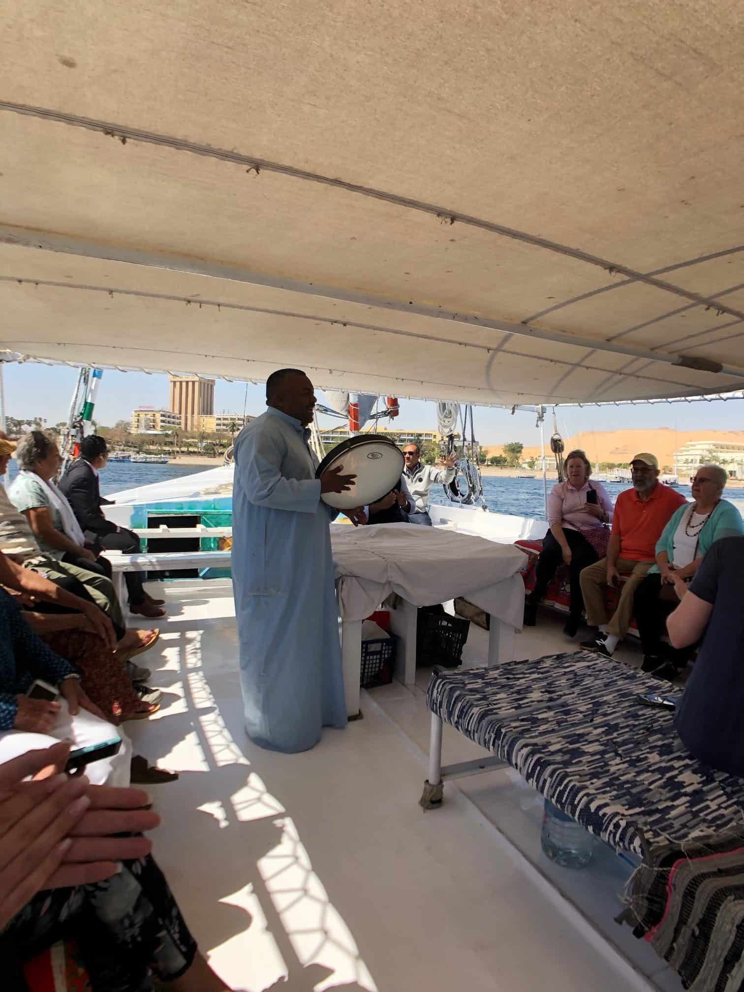 An Egyptian man in traditional garb plays a tambourine and signs traditional music on a Felucca tour in Egypt.