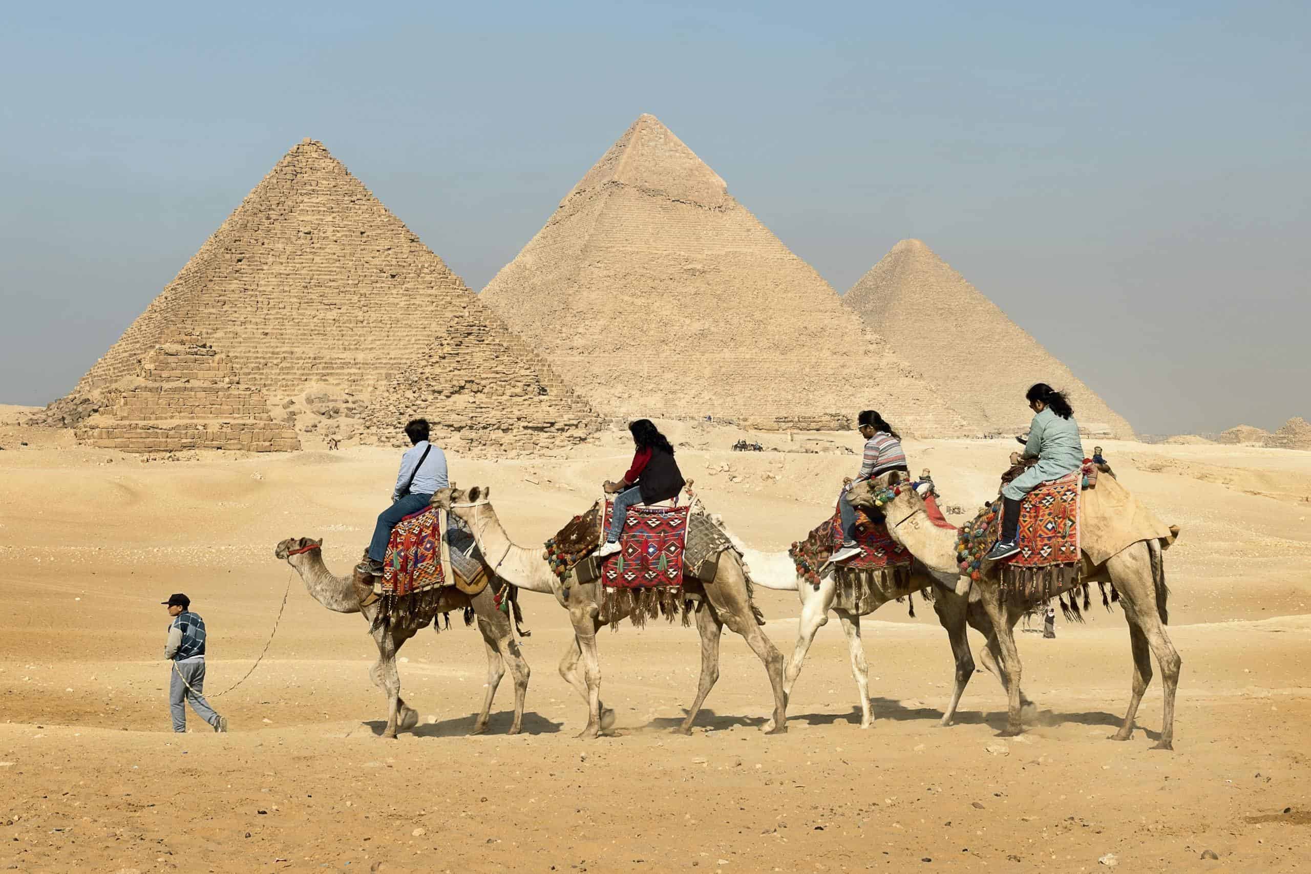 Tourists riding camels near the Great Pyramids of Giza, Egypt under clear skies.