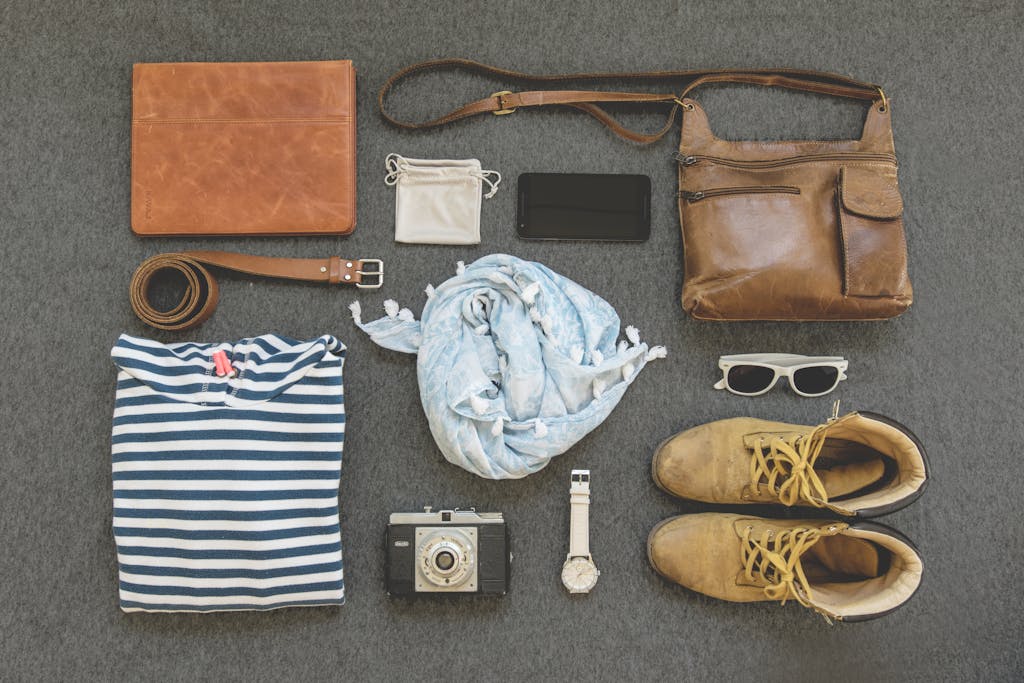 Travel essentials flat lay with leather bags, shoes, camera, and clothing.