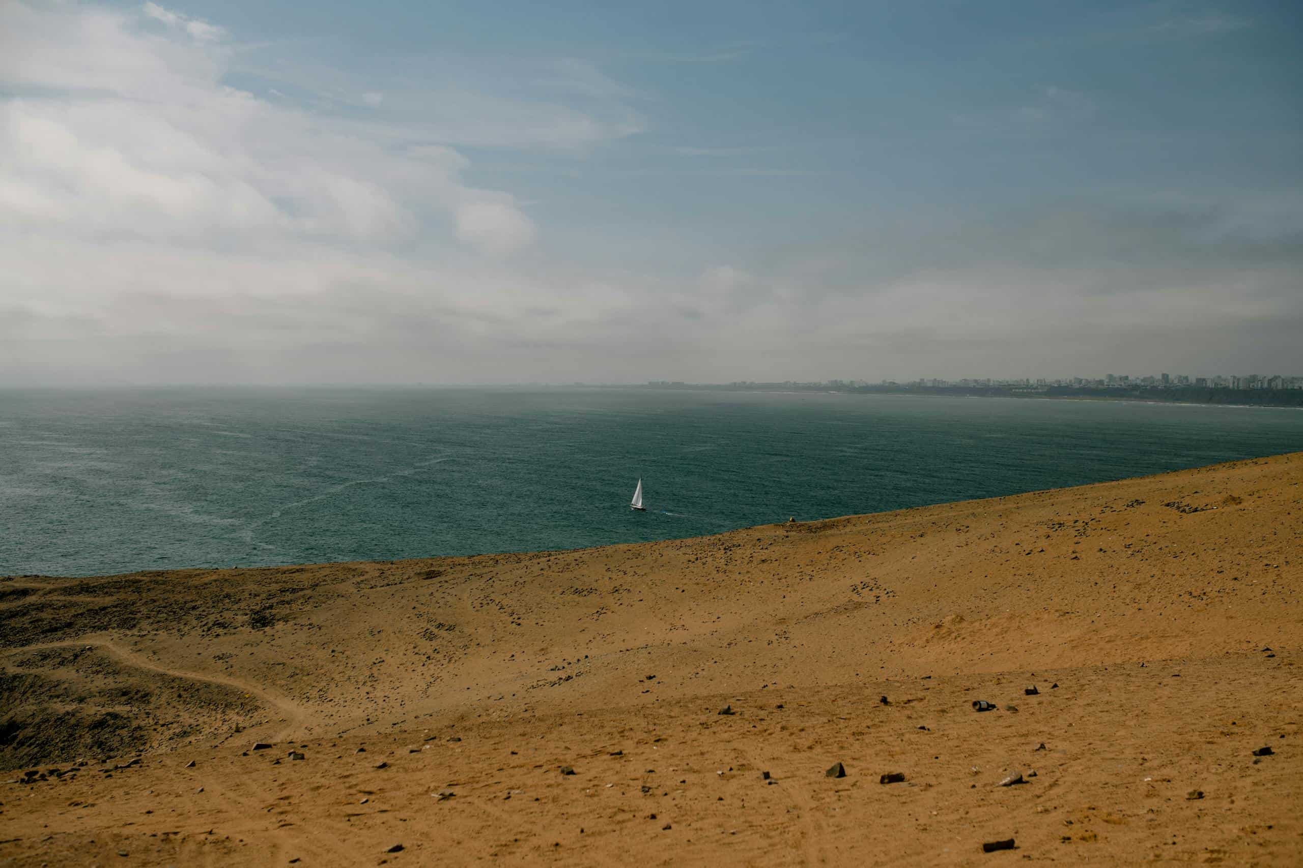 A serene view of a sailboat on the ocean, captured from the sandy shores of Lima, Peru.