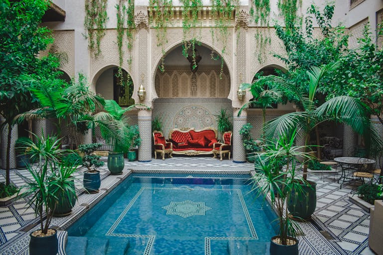 Elegant Moroccan courtyard featuring lush greenery and a decorative pool, perfect for a serene escape.