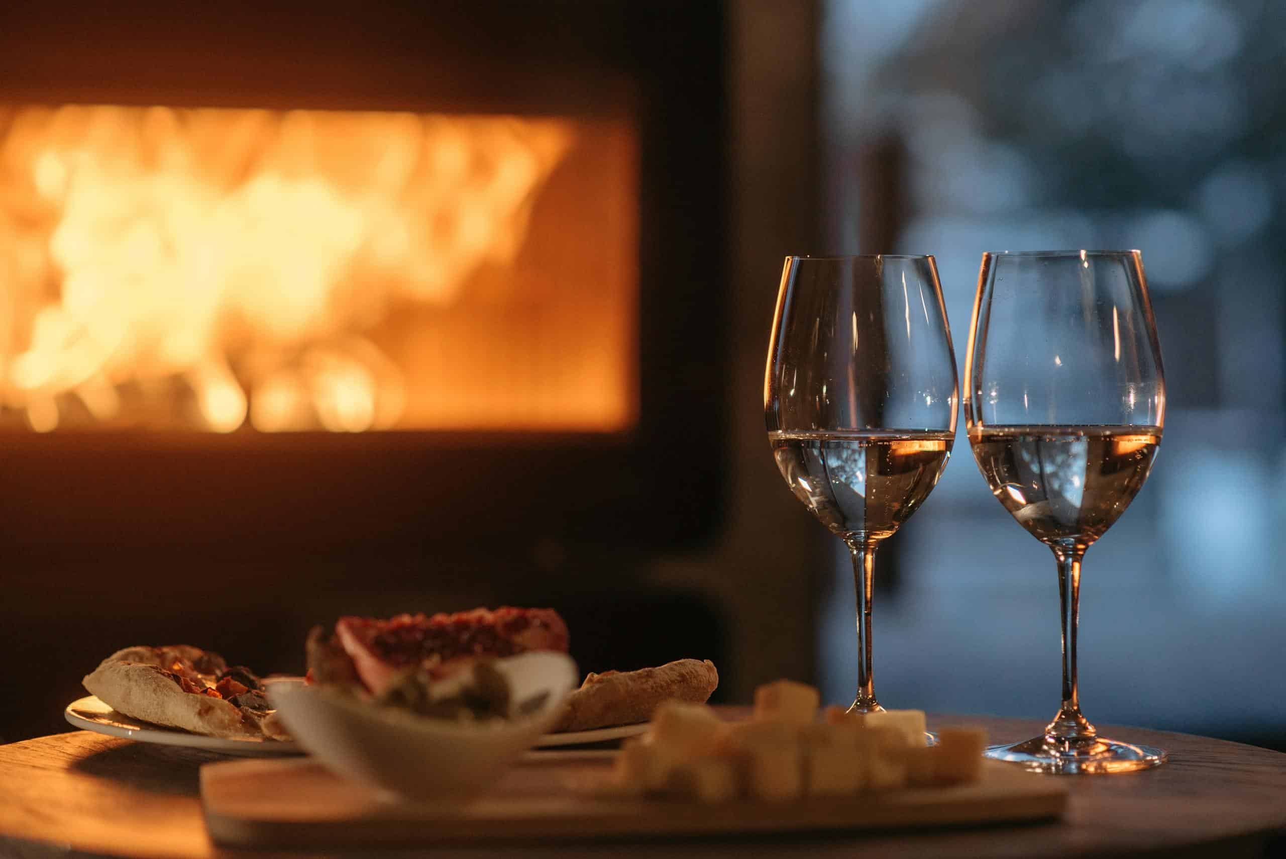 Romantic dining by the fireplace with wine and appetizers, perfect for a cozy winter evening.