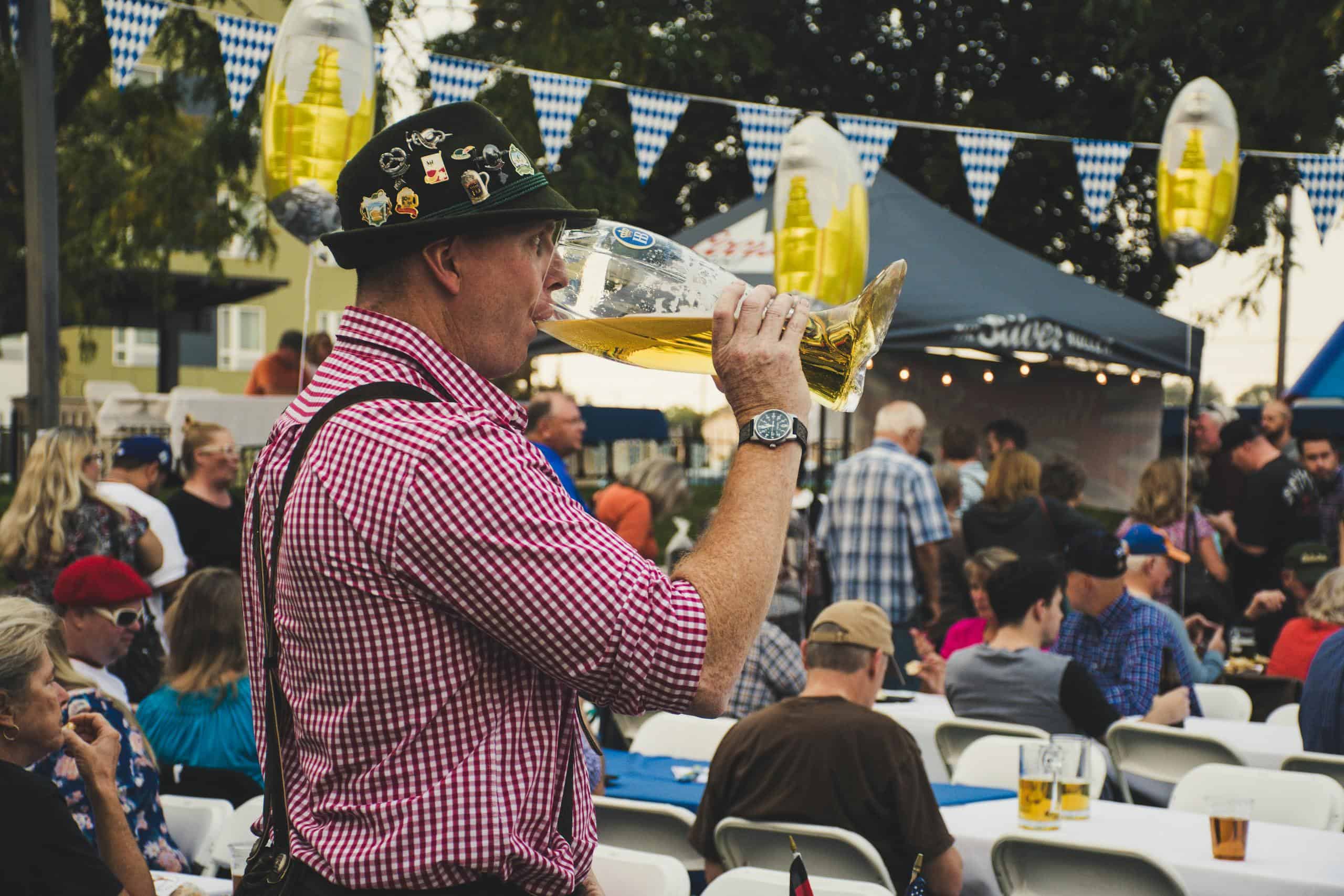 Man enjoying a large beer mug at an Oktoberfest celebration in Munich with a lively crowd.