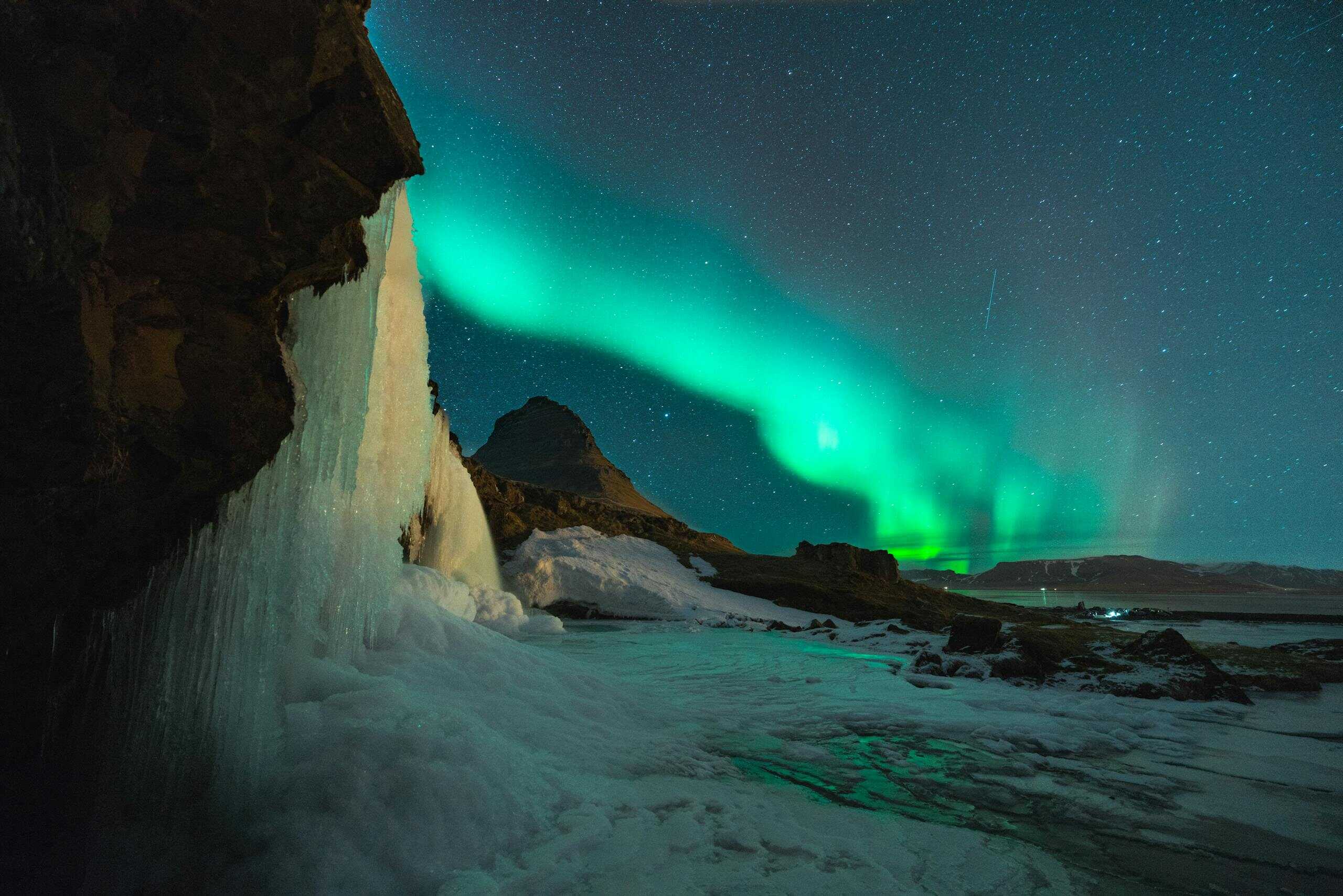 Stunning view of the Northern Lights over Kirkjufell mountain and frozen waterfall in Iceland.