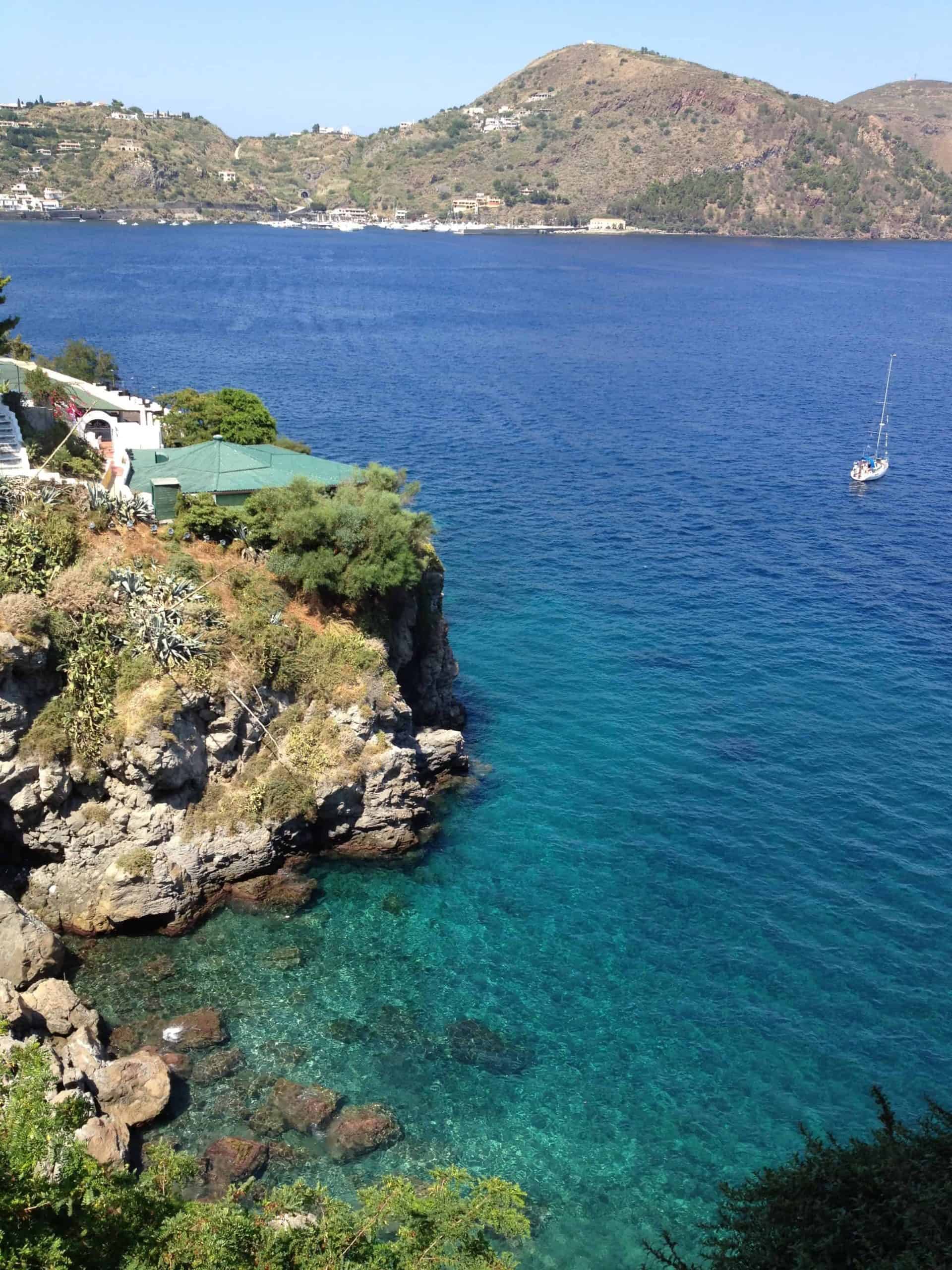 A sailboat floats in turquoise waters off the coast of the Aeolian Islands.