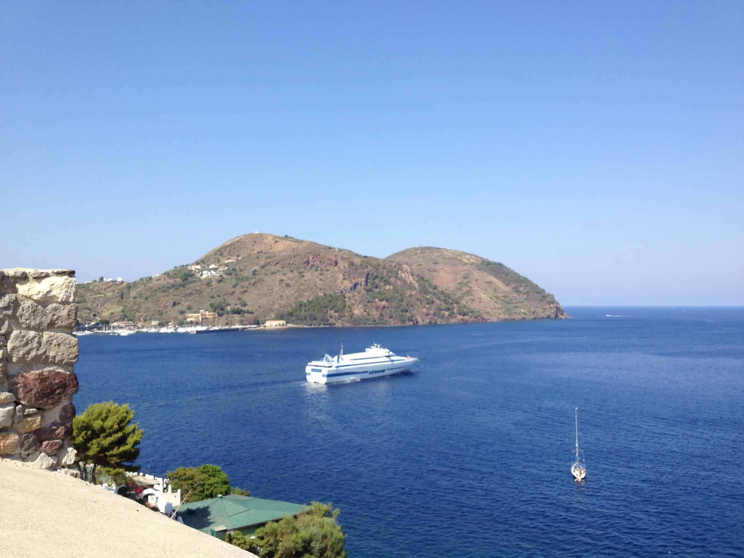 A boat sits in calm blue seas beside the Aeolian Islands.