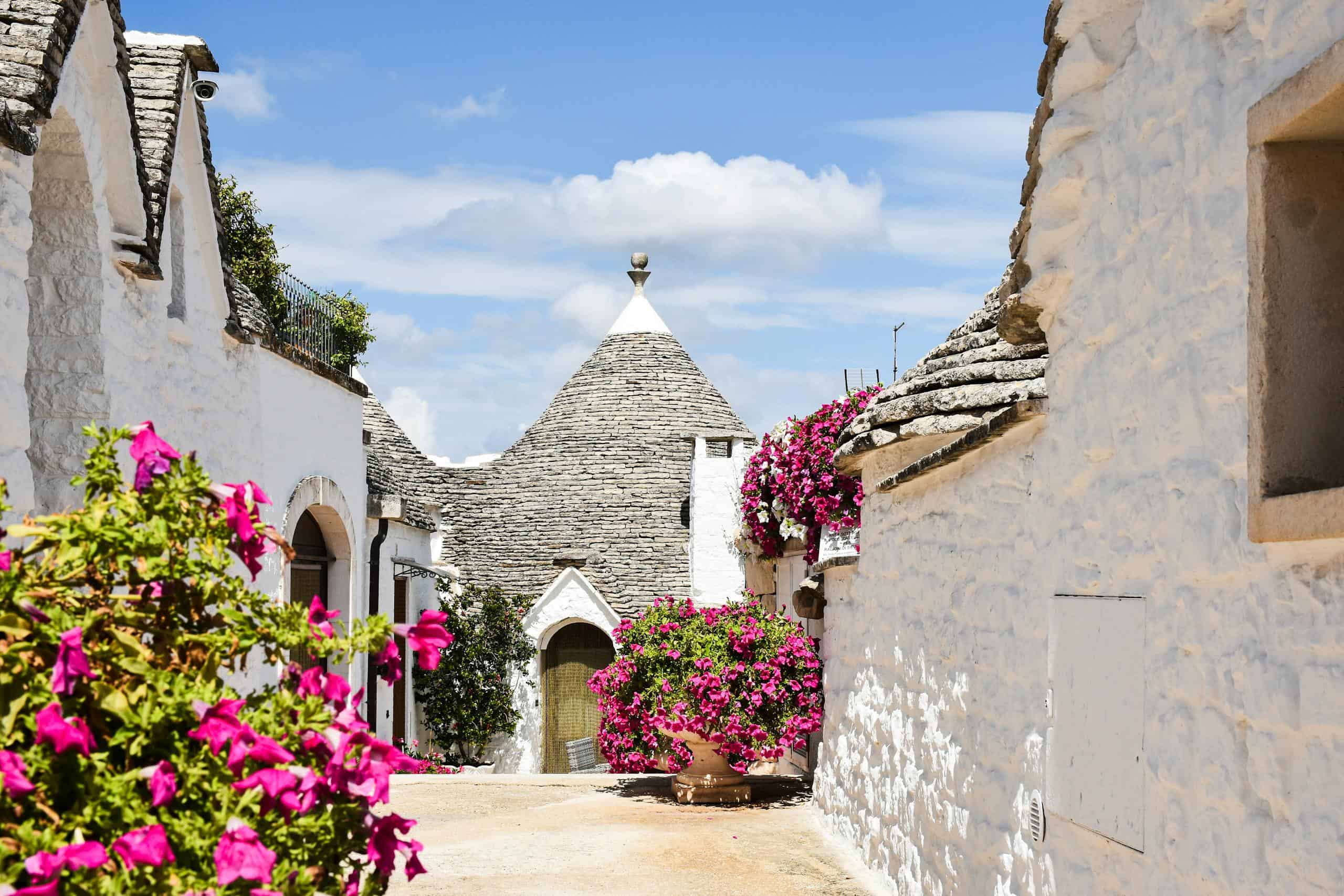 Charming trullo houses with vibrant flowers under a clear sky in Alberobello, Italy.