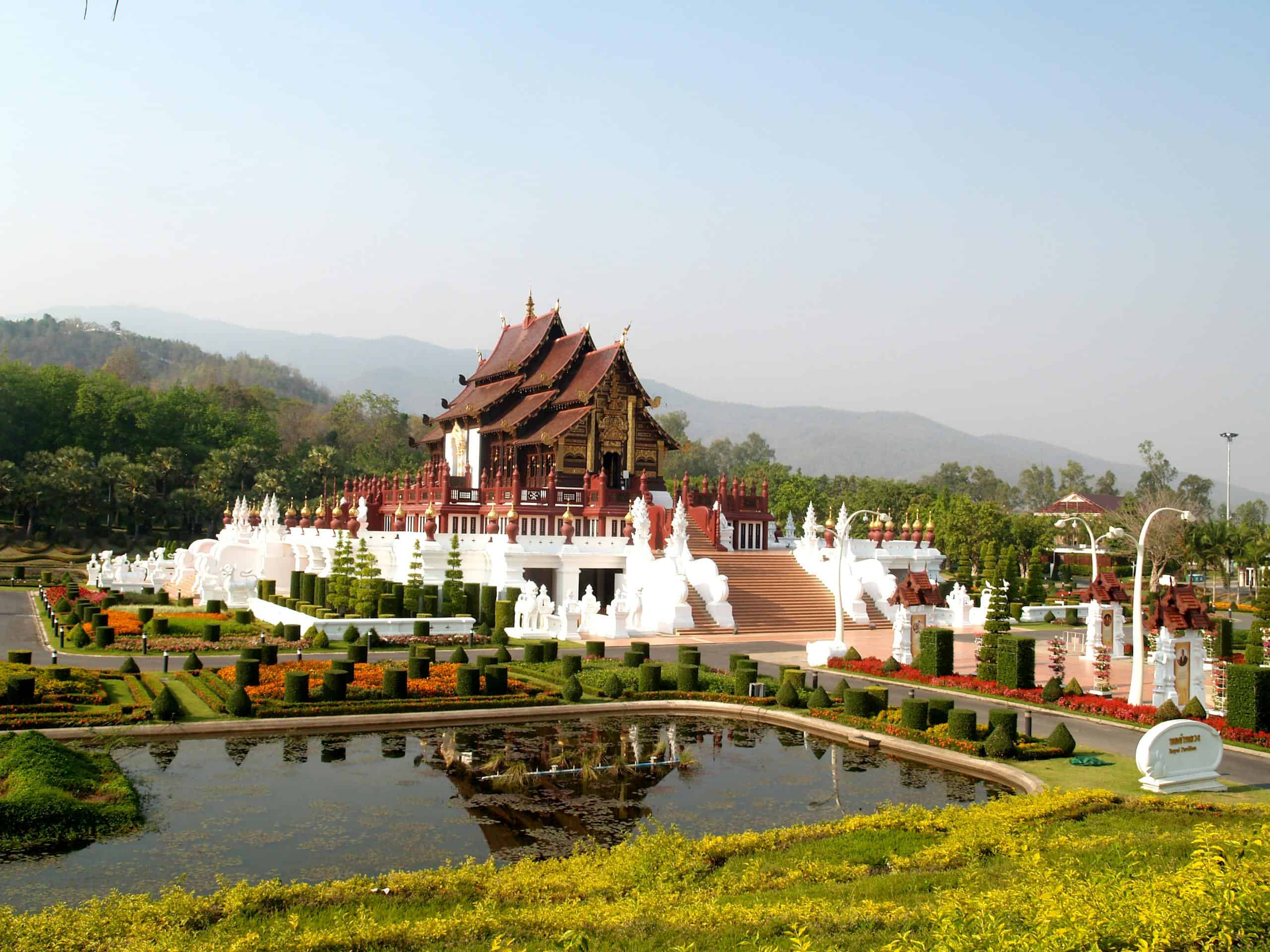 A beautiful Thai temple in Chiang Mai amidst lush gardens and a reflecting pond in daylight.
