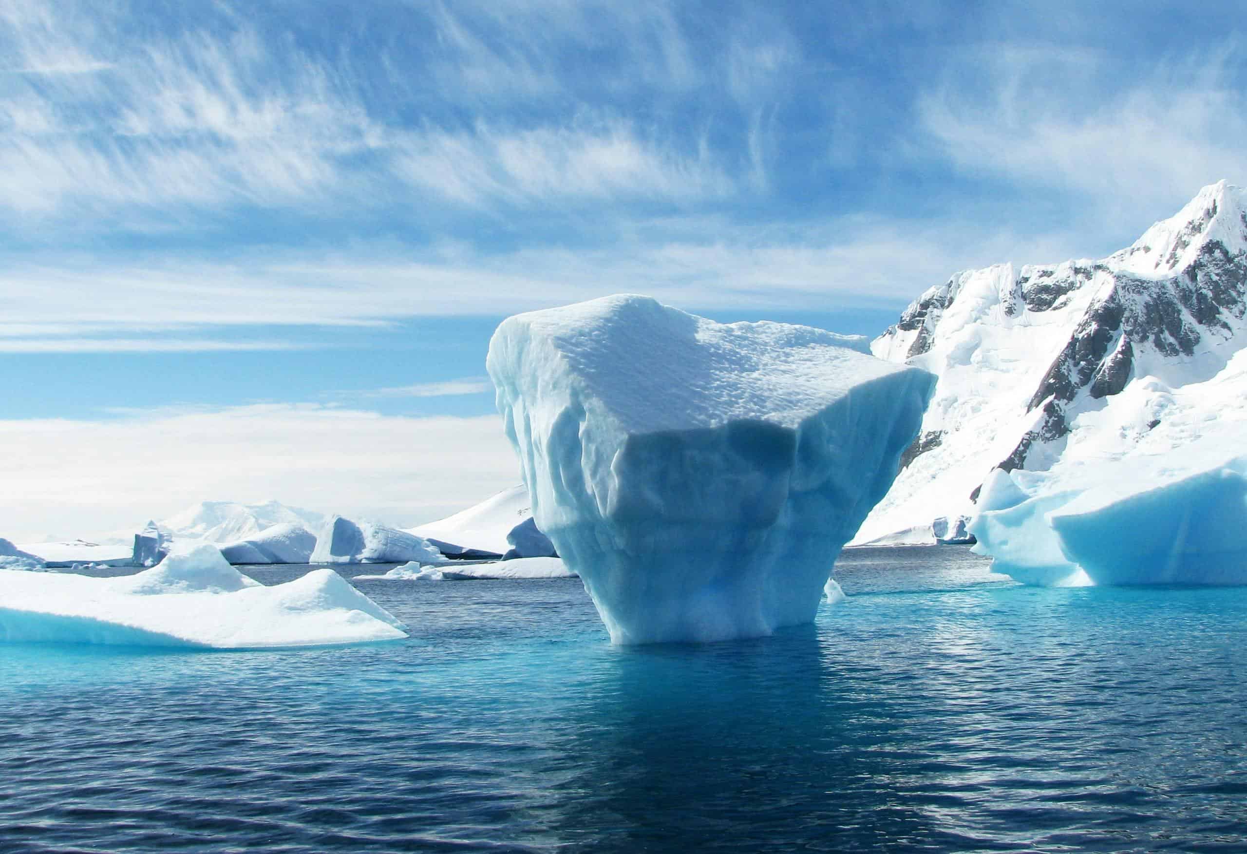 A stunning iceberg floating in the cold, pristine waters of Antarctica with a backdrop of snowy mountains.