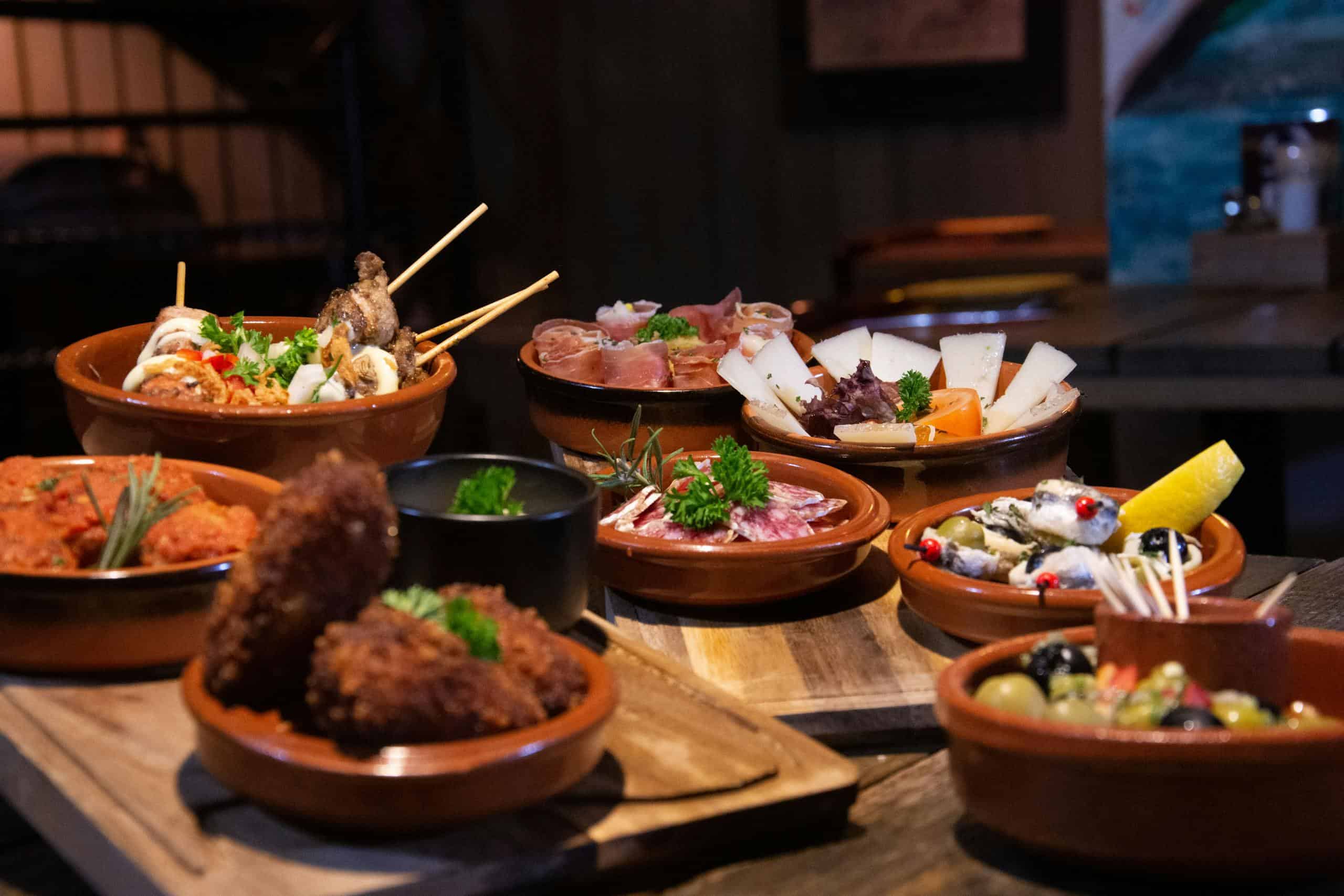 An inviting spread of various tapas dishes elegantly arranged in a cozy indoor restaurant in San Sebastian, Spain.