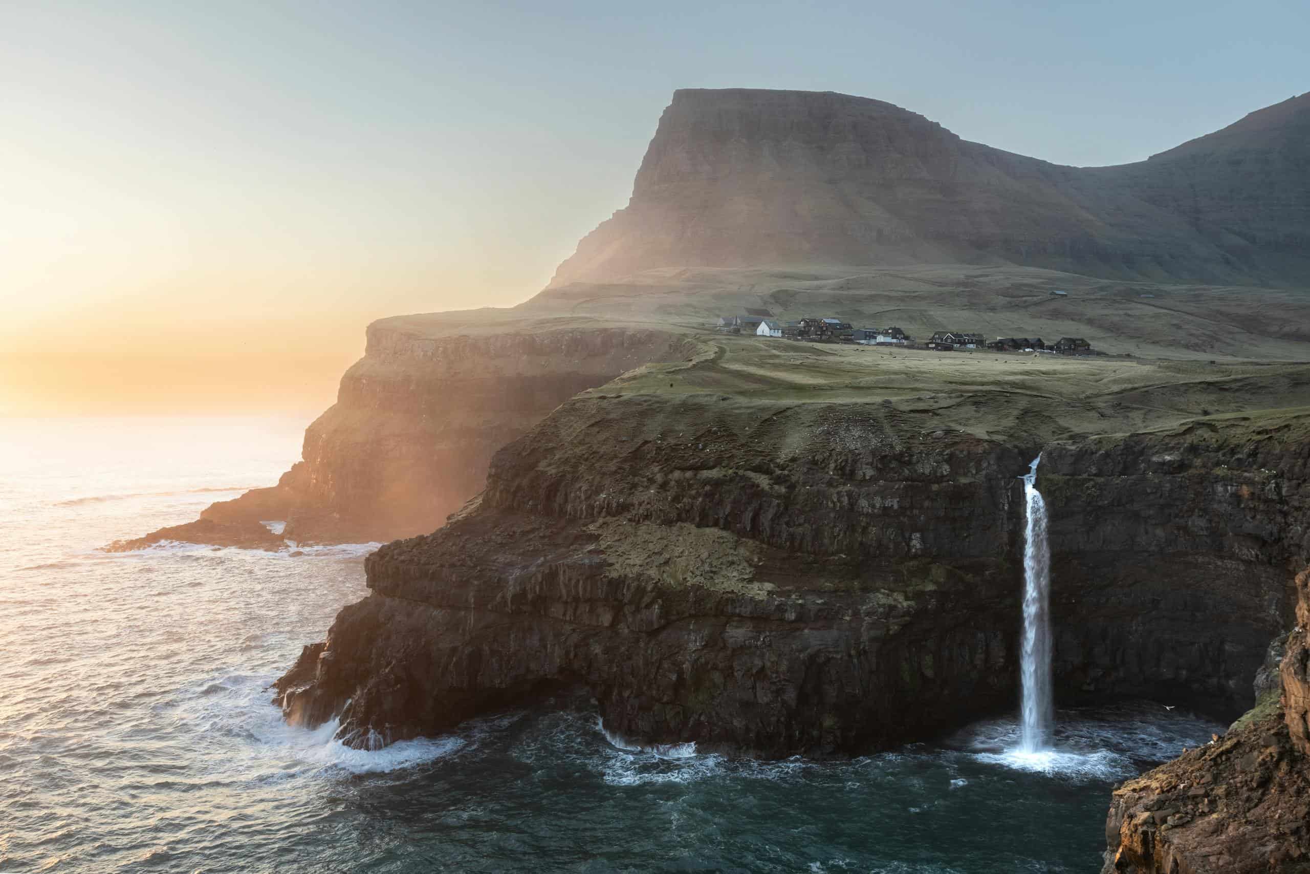 Breathtaking view of a waterfall flowing into the sea on the Faroe Islands' rugged cliffs during sunrise.