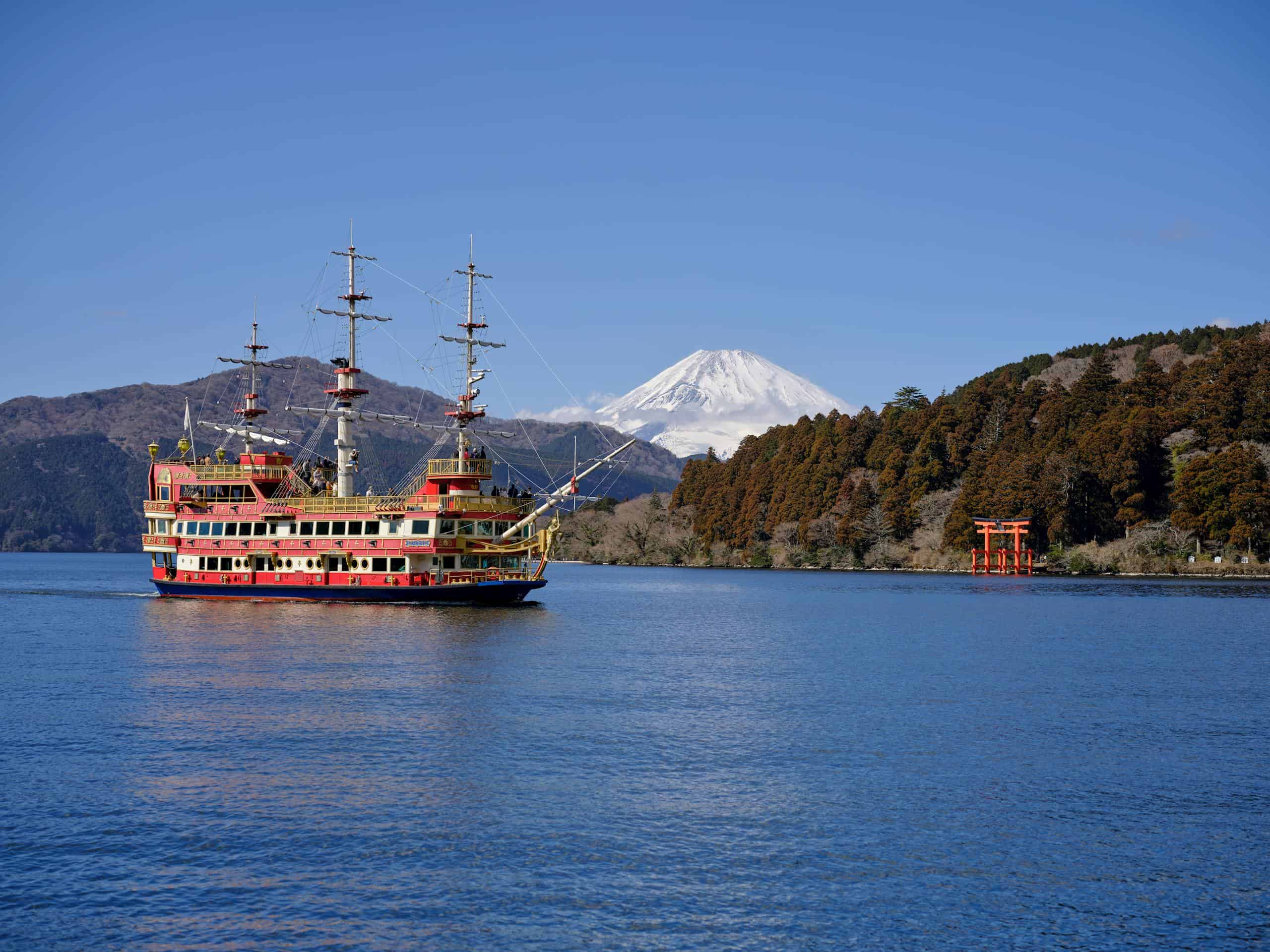 Colorful pirate ship sailing on Lake Ashi with Mount Fuji in the background and a Torii gate along the shore.