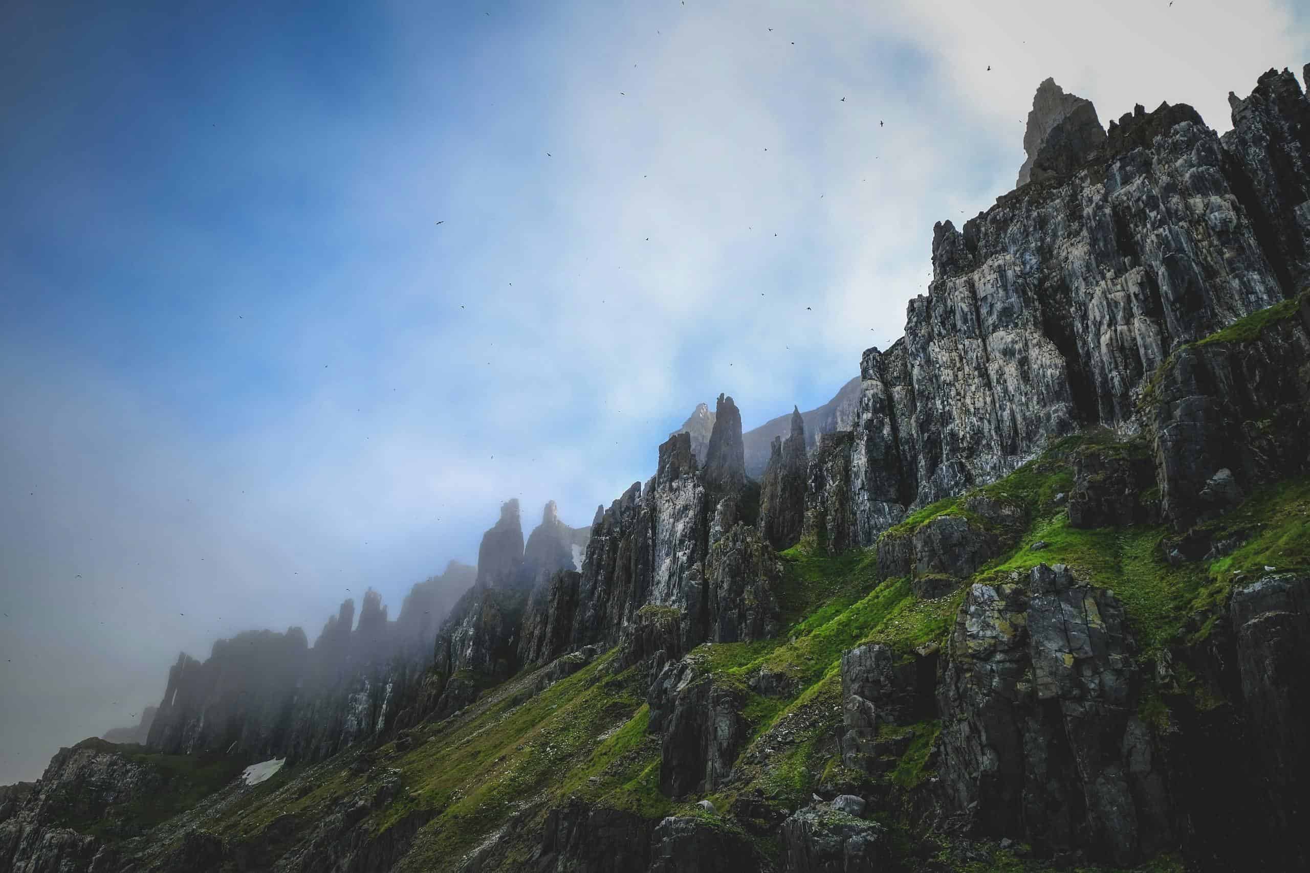 Dramatic mist-covered rocky cliffs with lush green moss in Svalbard, Norway.