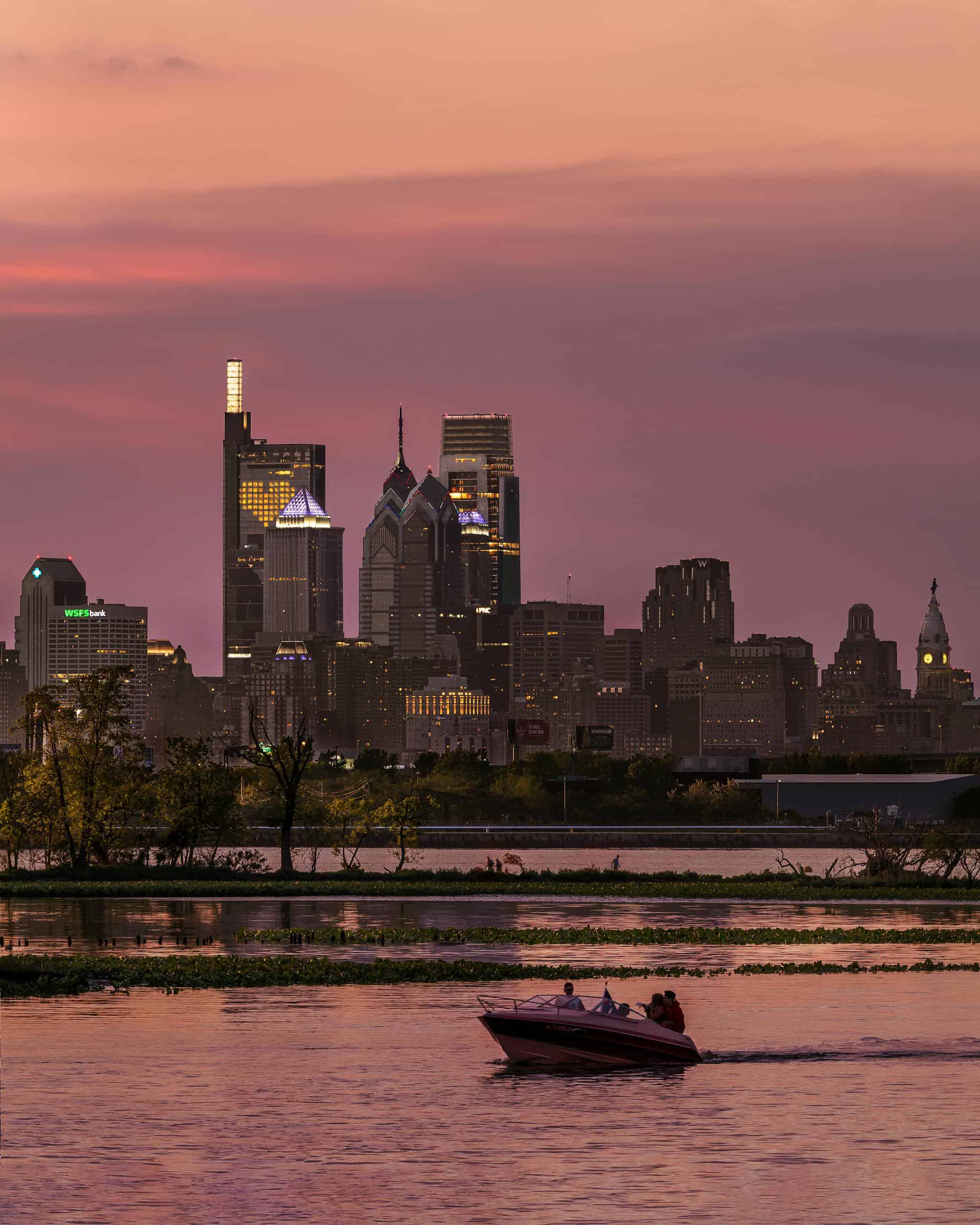 Dramatic skyline of Philadelphia at sunset with a motorboat on the water, capturing urban serenity.