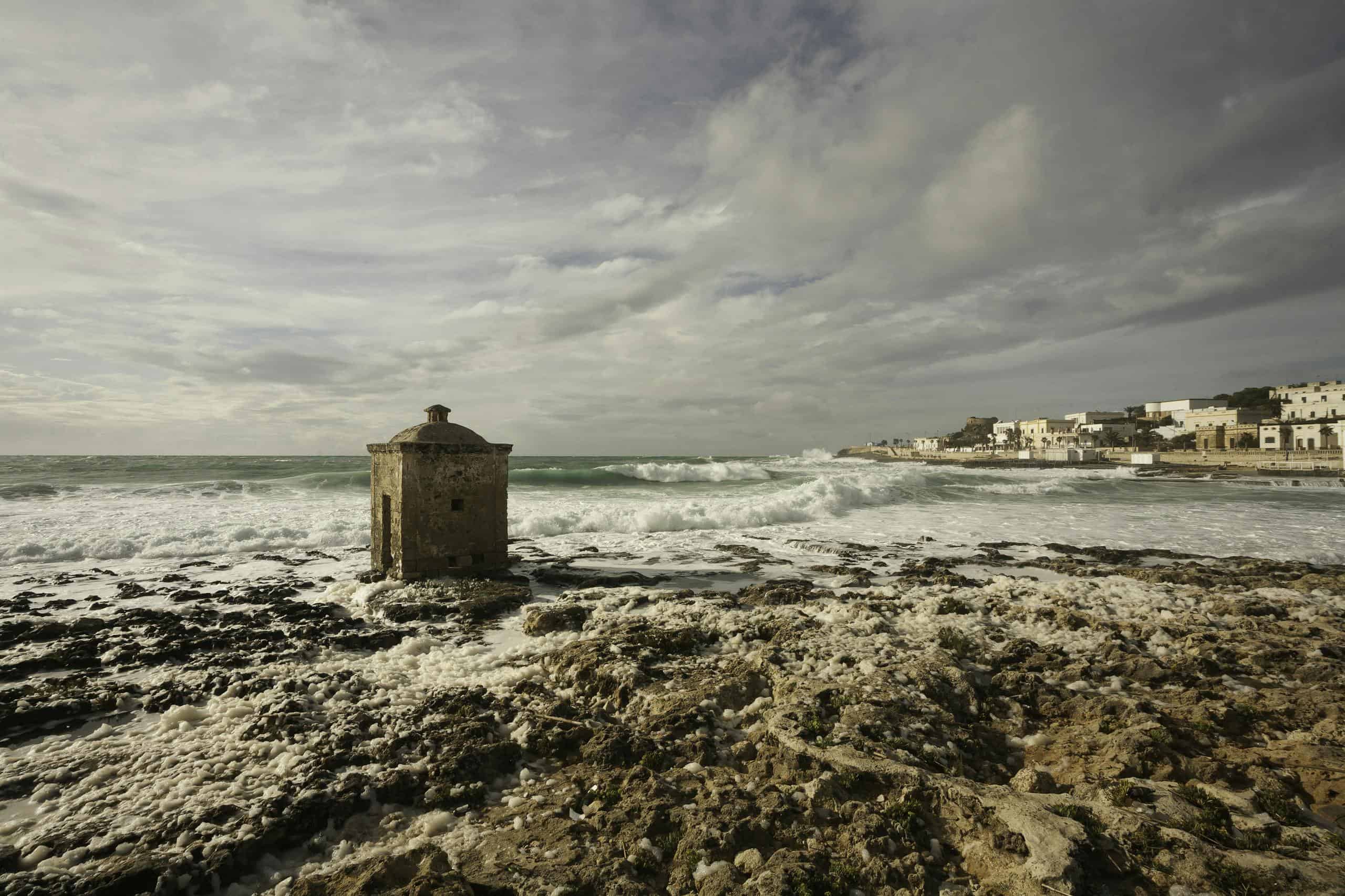 Explore the rugged coast of Santa Maria di Leuca with its iconic stone structure and crashing waves.
