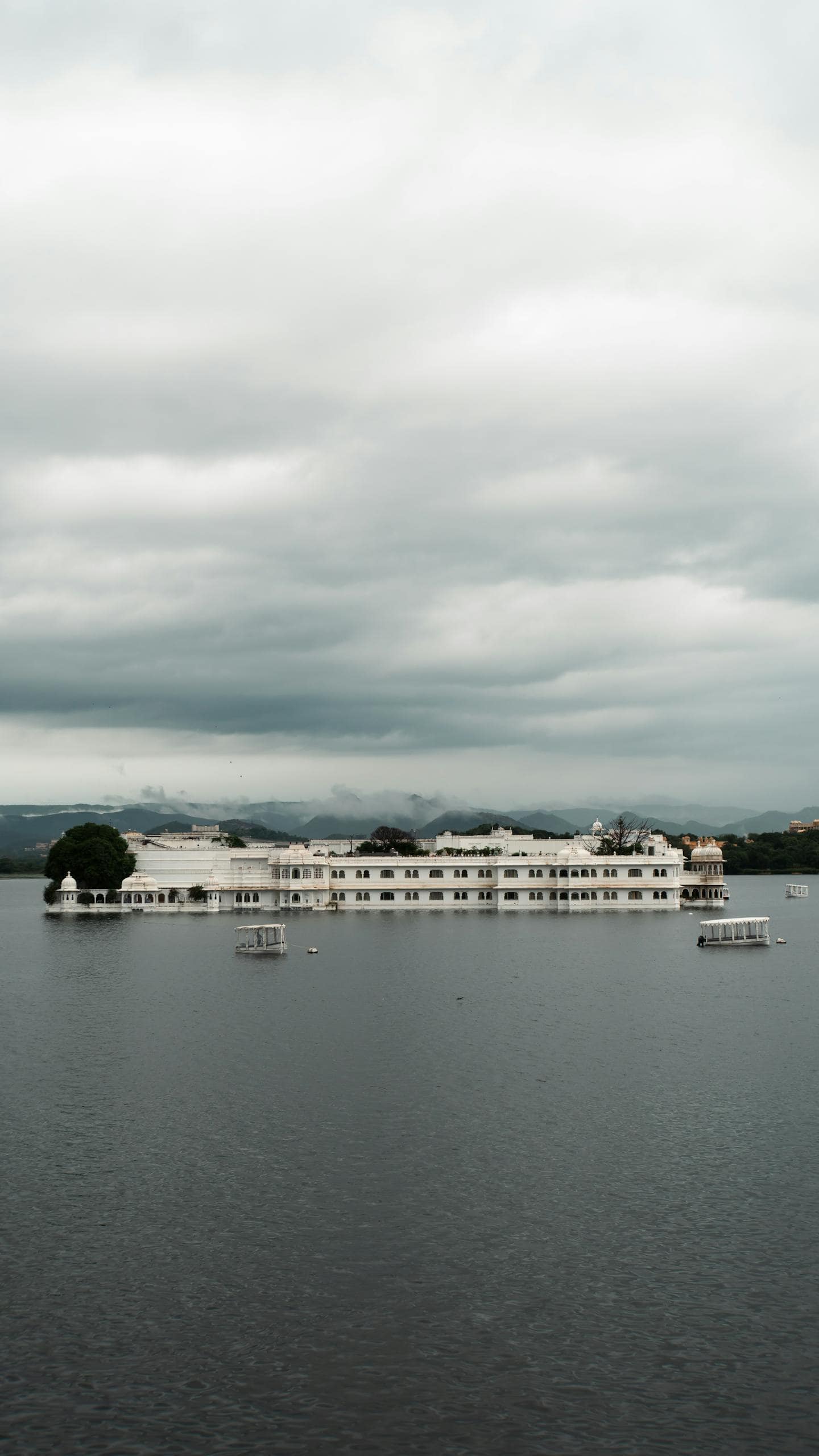 Scenic view of Udaipur's Lake Palace on a cloudy day, capturing serene beauty.