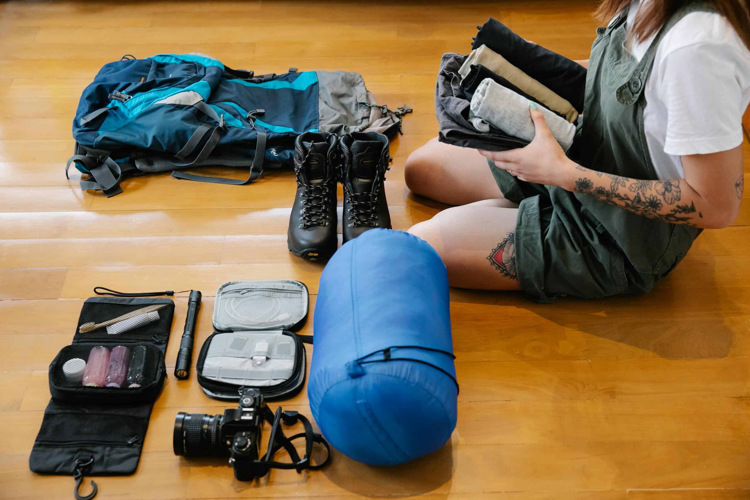 Woman organizing gear and clothes on wooden floor indoors, preparing for an adventure.