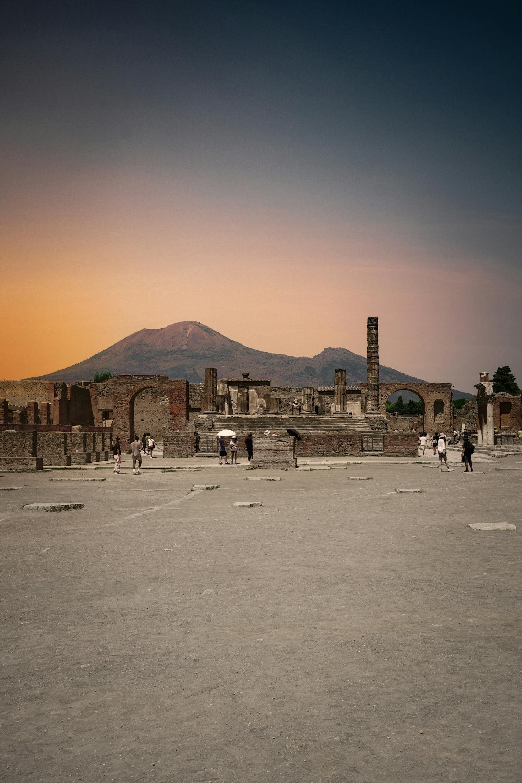 Explore the historical ruins of Pompeii at sunset with a view of Mount Vesuvius in the backdrop.