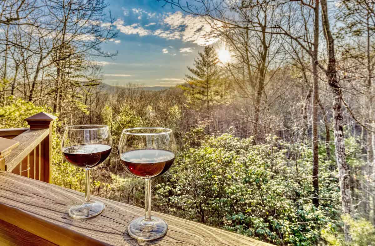 Two wine glasses on a railing with a romantic view of the mountains in the distance.
