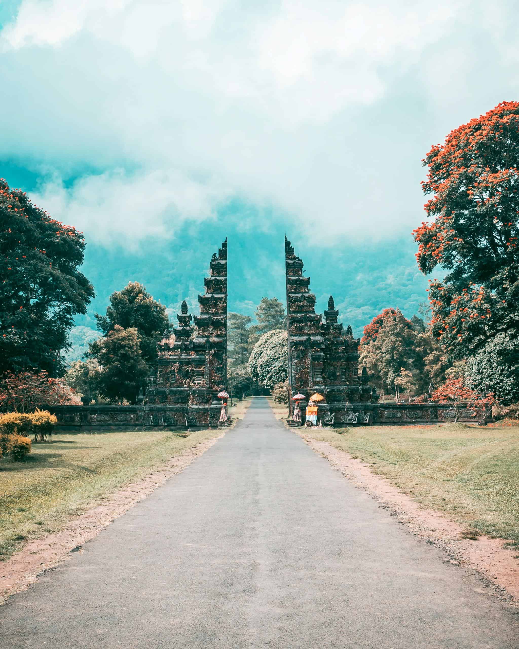 Majestic Balinese gate amidst a lush, tropical landscape and towering mountains, under a bright sky.