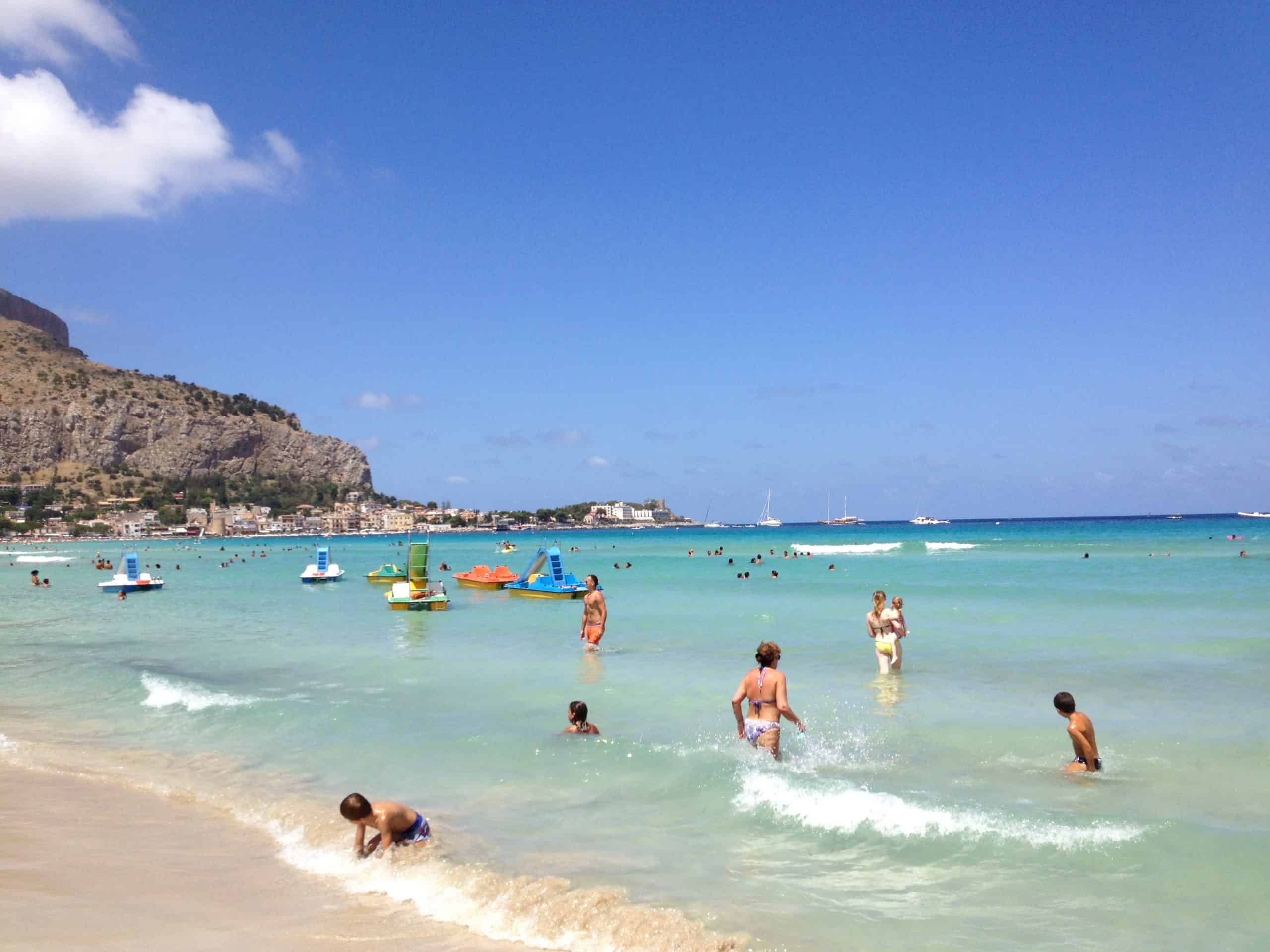 A beach in Italy with turquoise water and people standing or playing in the surf.
