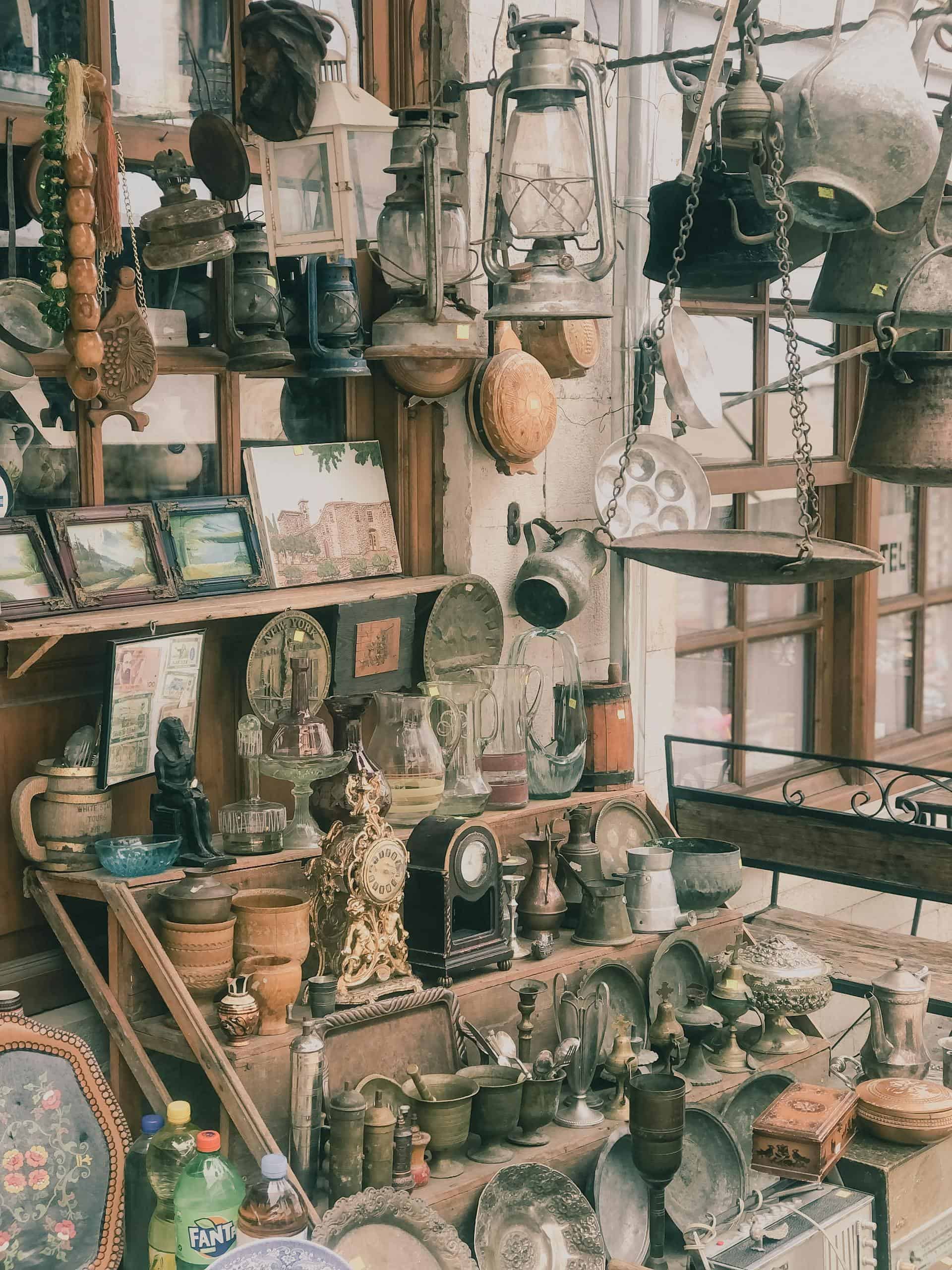 A collection of vintage antiques displayed in a shop window with varied items like lanterns and pottery.